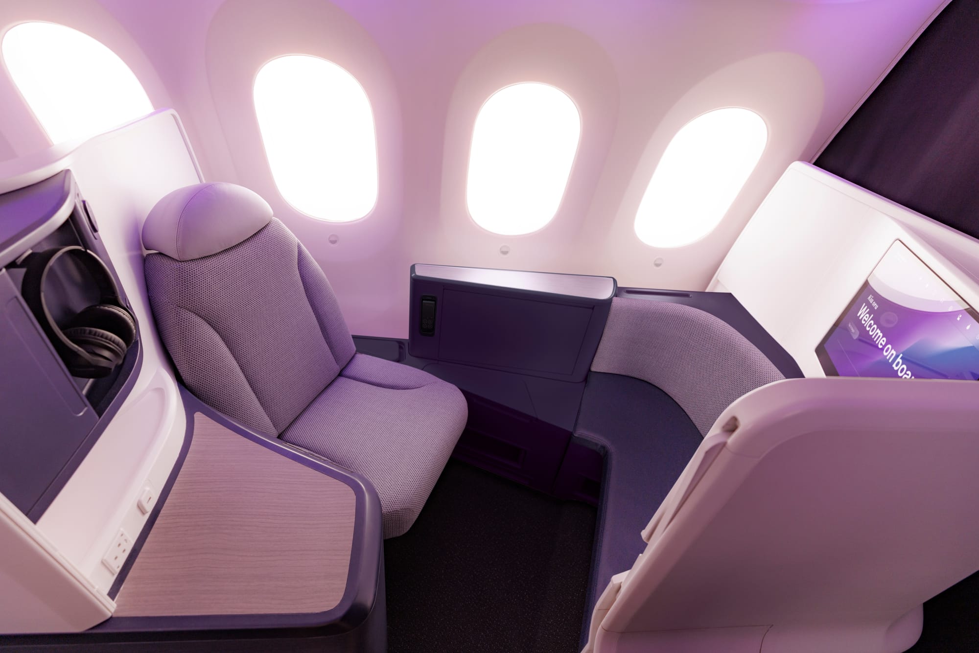 Interior, airline cabin. A front-row business-plus suite with a visible door that is open. There's no seat in front, so the area is opened up for a buddy diining seat.