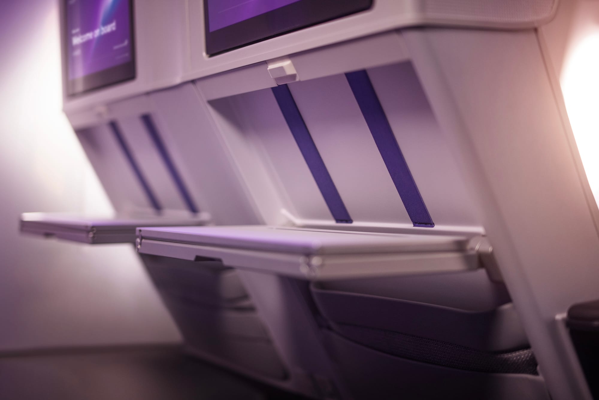 Closeup, premium economy seat table. Two stretchy straps are fitted vertically in the negative space created when the table opens.