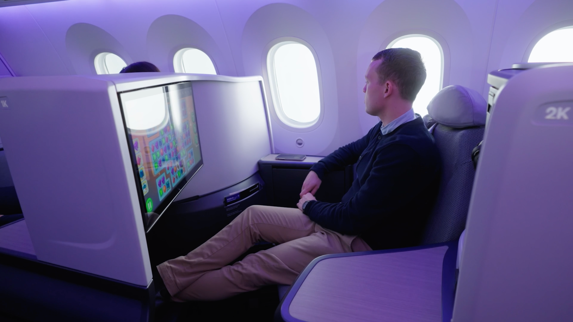 Interior, airline cabin. A man sits in a business class seat (Air NZ new Business Premier), looking away from the camera.