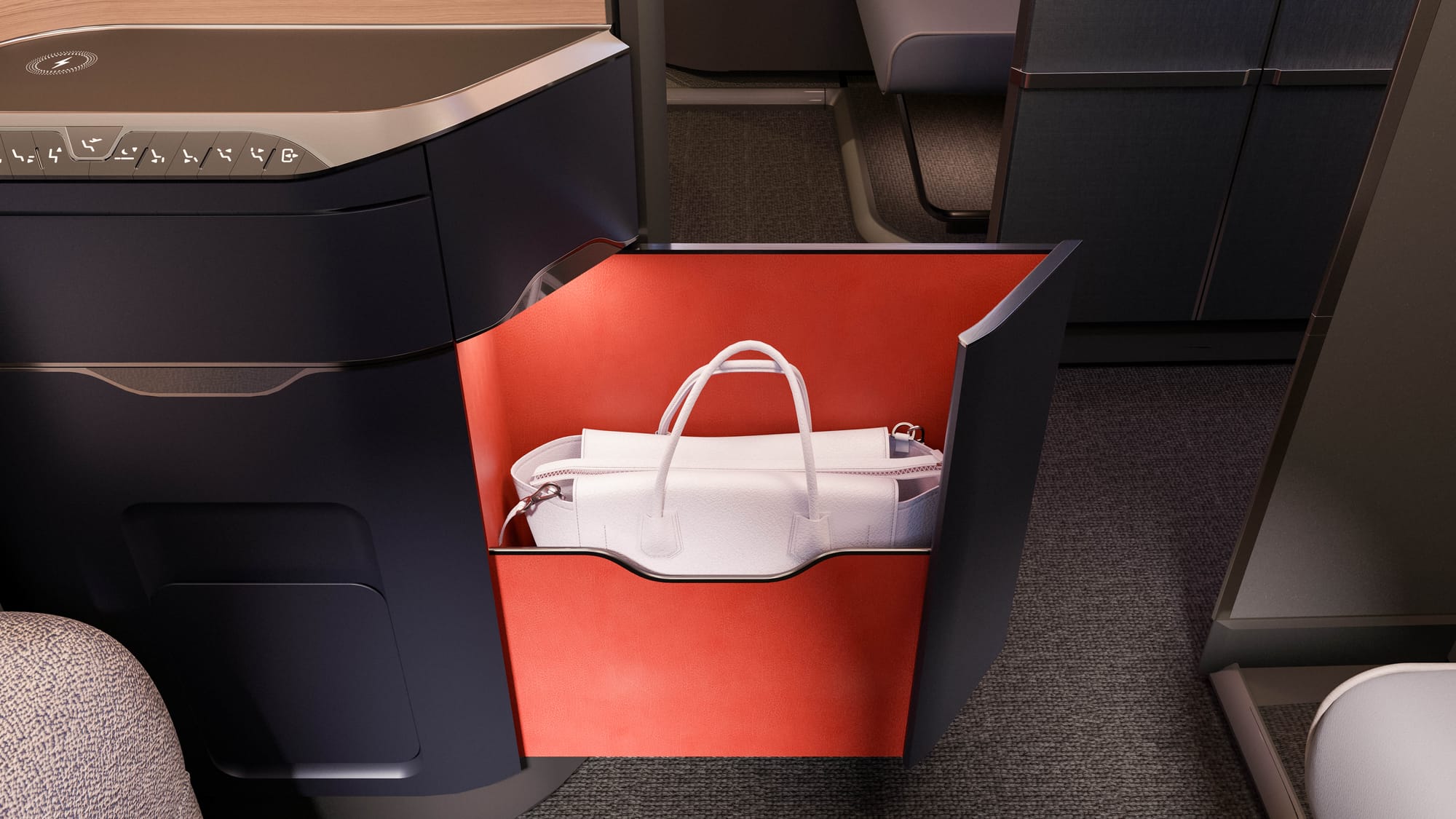 Close up, airline seat. An cabinet with an angled front surface extends to form a pointed shape rather like the number 7. Inside, the cabinet is bright red, with a medium-sized white leather tote bag sitting inside.