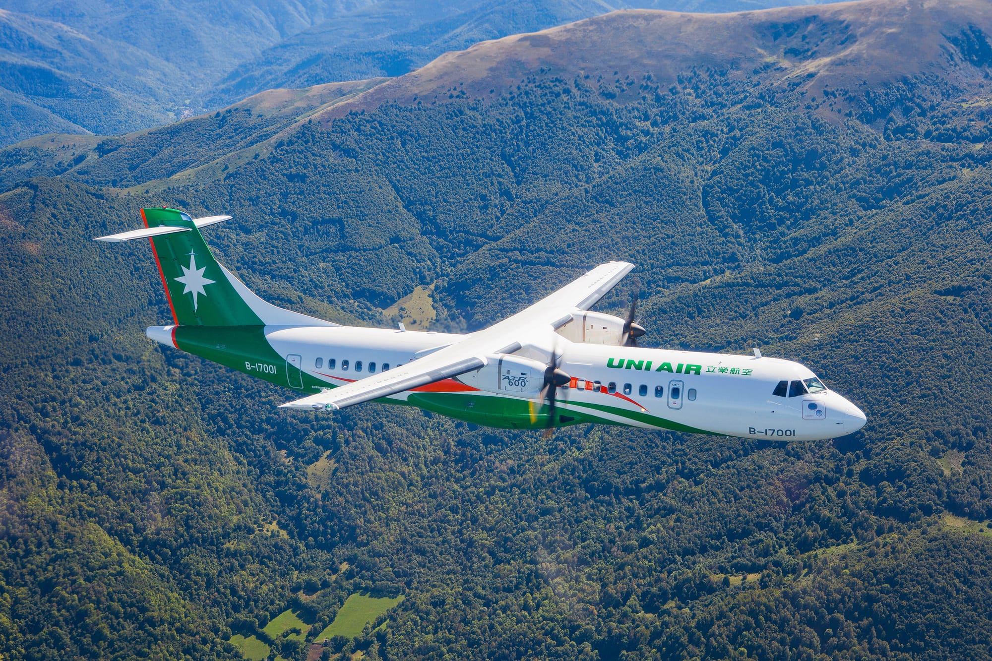 Airplane in flight: a small UNI Air white and green livery ATR 72, with white star on green tail, over some mountains