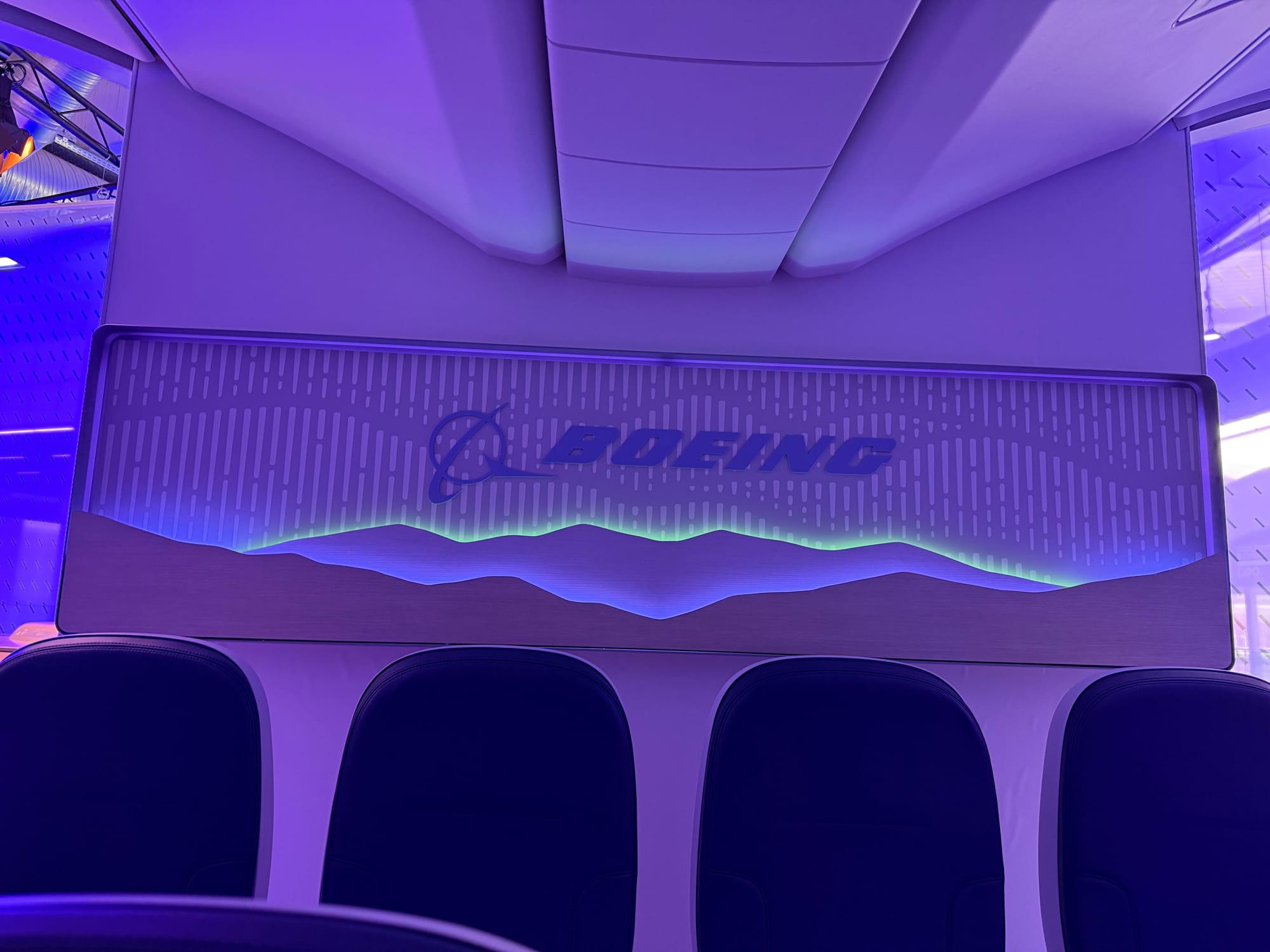 Closeup on a rear cabin monument branding panel: the Boeing logo, then backlit mountains and an dots-and-dashes icicle pattern echoing more mountains.