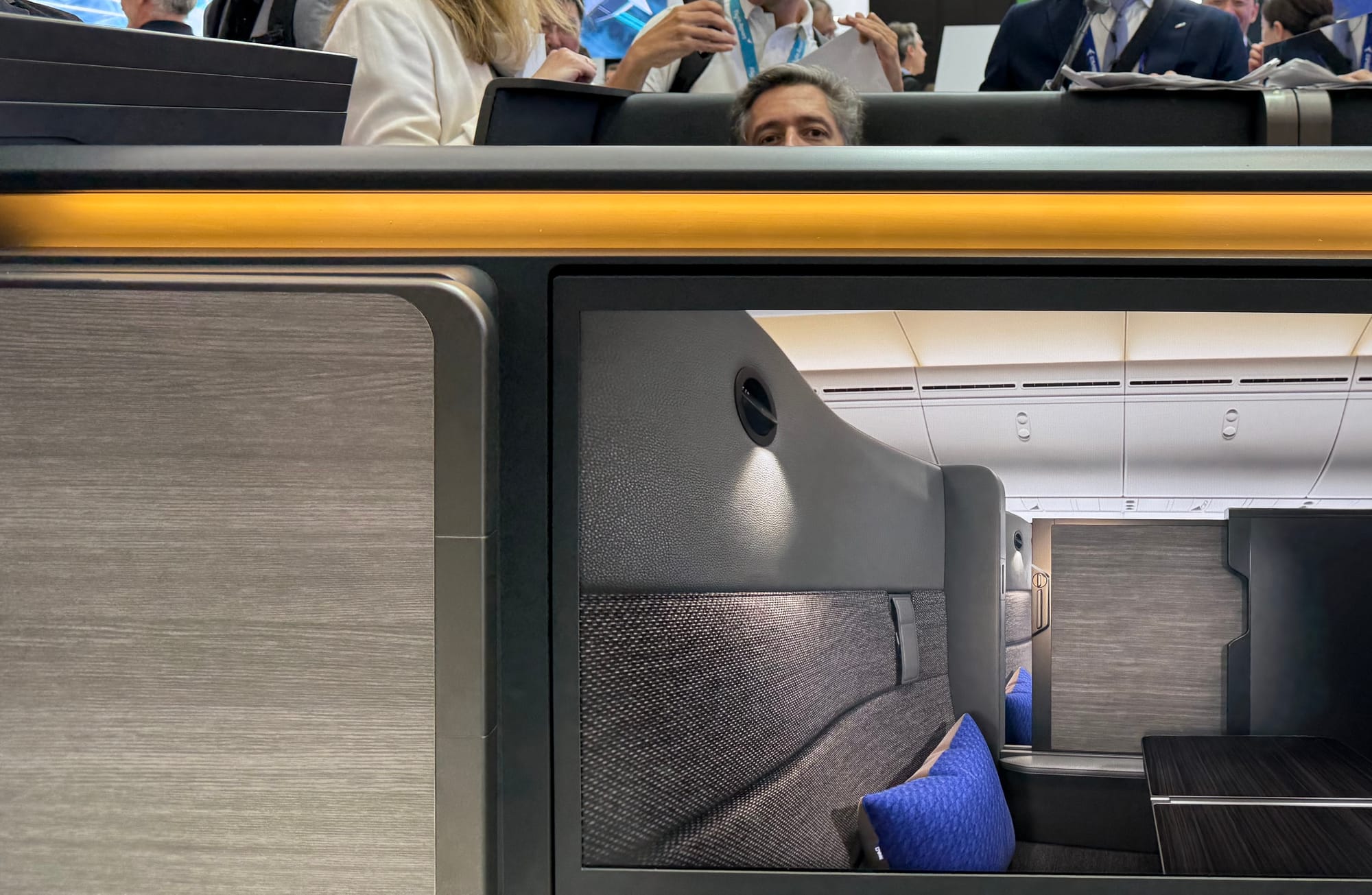 A closeup over the top of the centre section between two seets, with a man's eyes visible in the seat opposite.