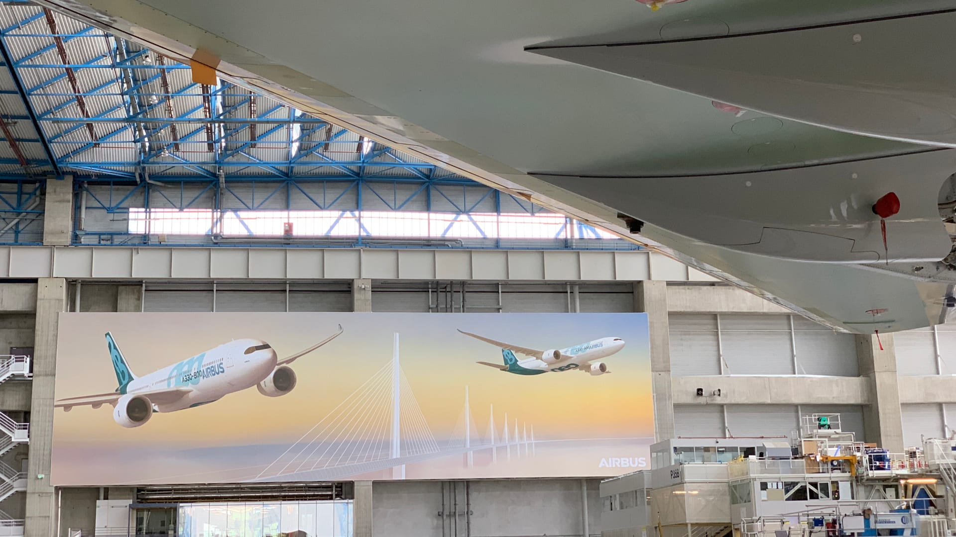 Interior, A330neo factory, under a wing, with two large images of the A330neo on the factory wall.