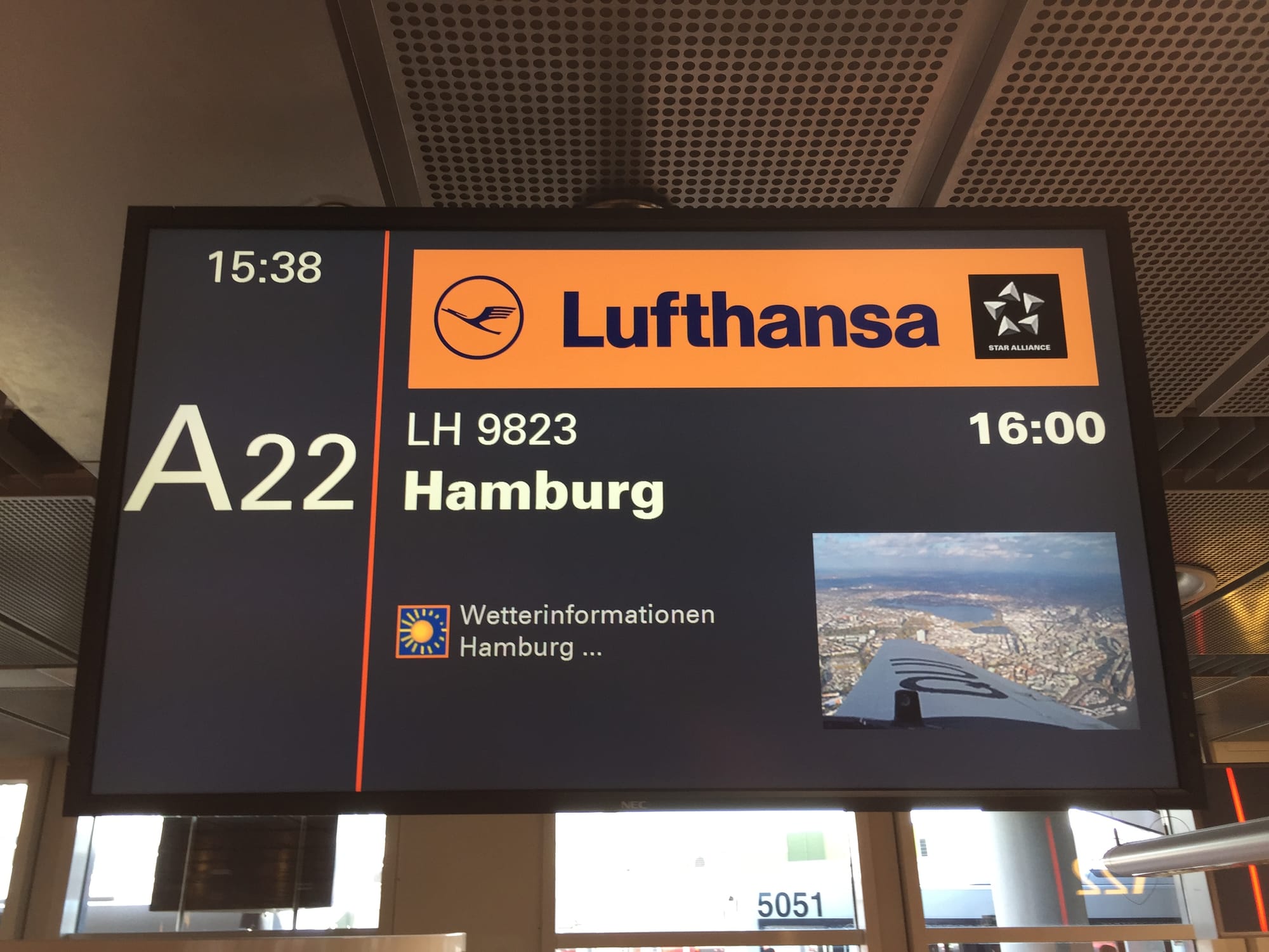 Closeup of the departure screen from Hamburg Airport, gate A22, with the golden Lufthansa livery and a picture of Hamburg overhead from D-AQUI's right side