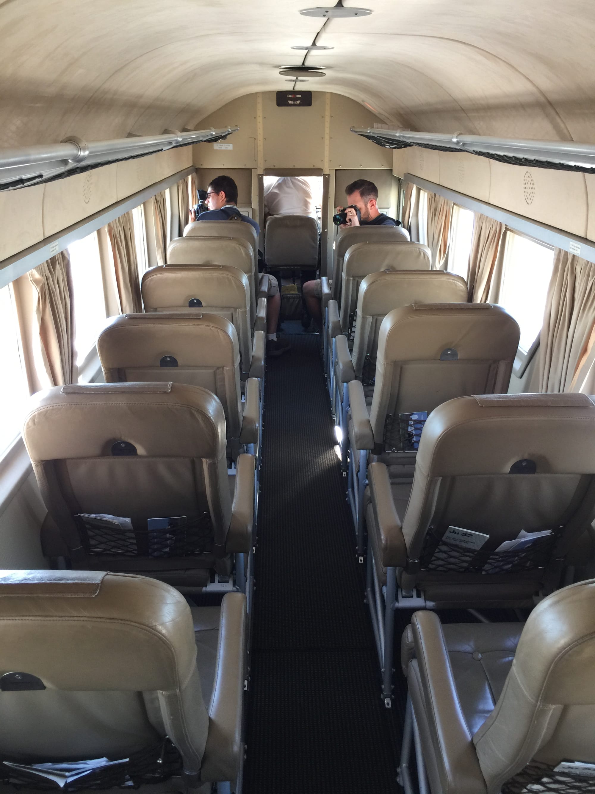 A photo of the cabin from the rear, with a pilot in the third flight deck seat and two men taking photographs with SLR-type cameras in the two front seats.