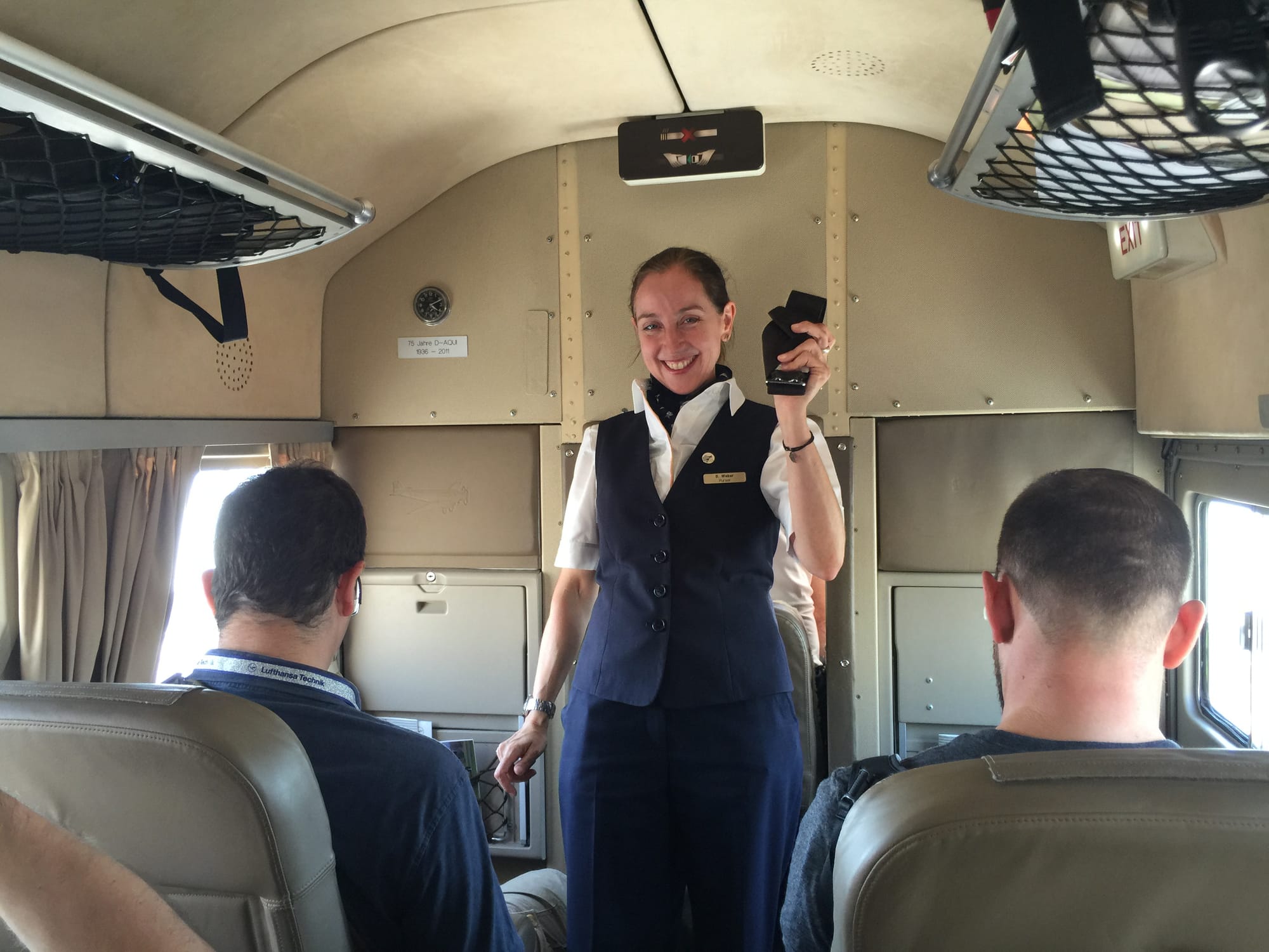 Essentially the same shot as previously, but with a smiling flight attendant holding a demonstration seatbelt.