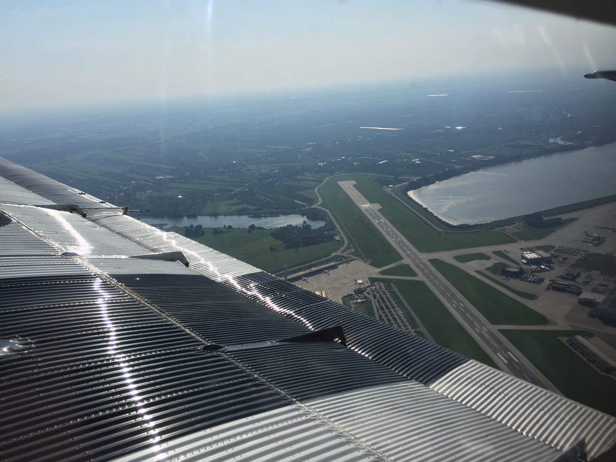 Window shot of from the air, looking slightly backwards with the long Airbus runway at Finkenwerder on the ground.