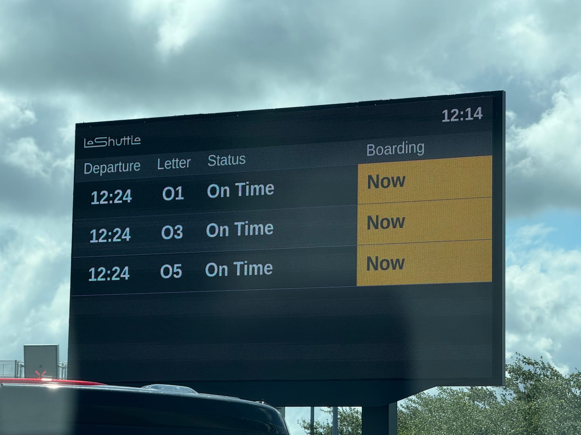Large LeShuttle display board outside, with the 1224 departure for letters O1, O3 and O5 marked as "On Time" with Boarding "Now".