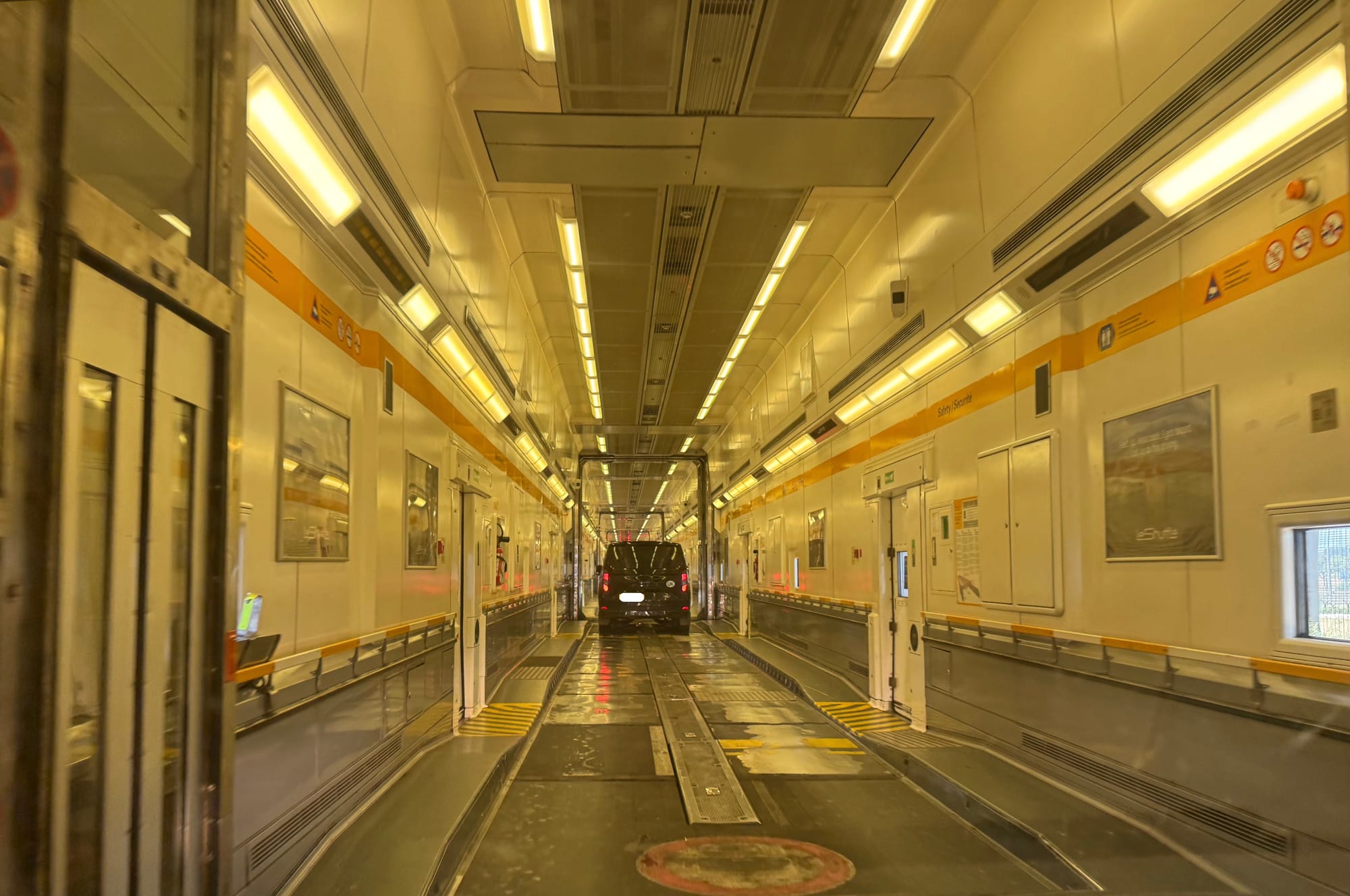 Interior, auto train, one level. A high-roofed series of train cars separated by doors (which are currently open and mostly hidden). Lighting is yellowish. There are escape doors and occasional small windows.