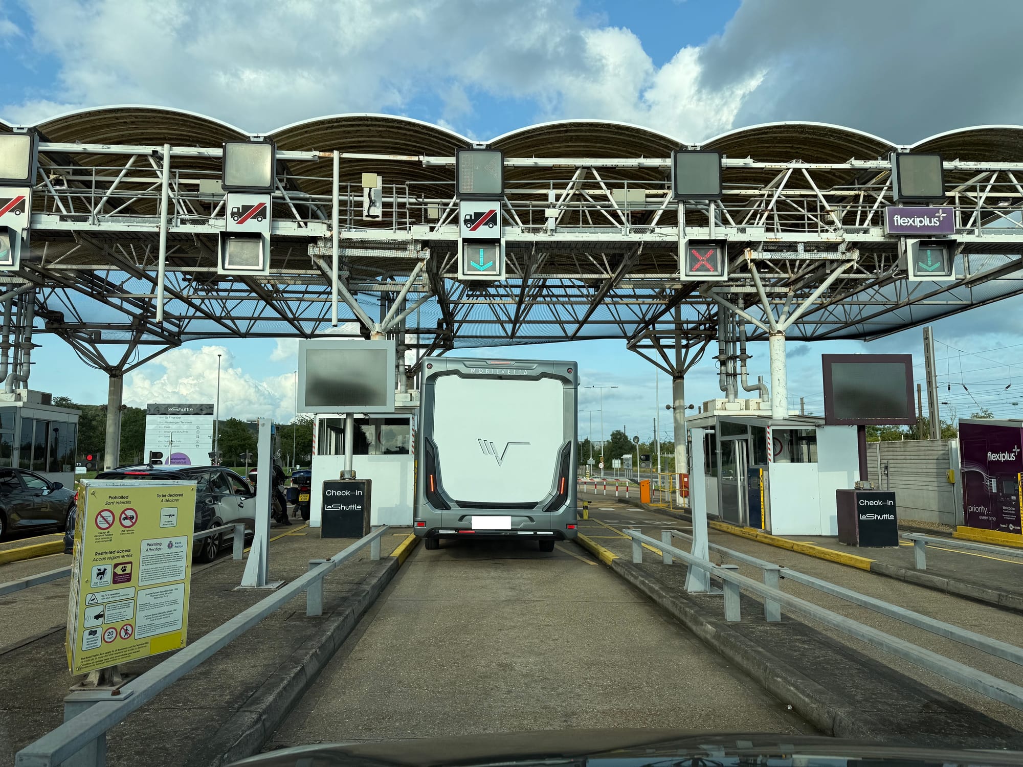 Tollbooth-style checkin area, with a few cars in other lanes and one motorhome in front. To the right is Flexiplus checkin, which looks much like regular checkin.