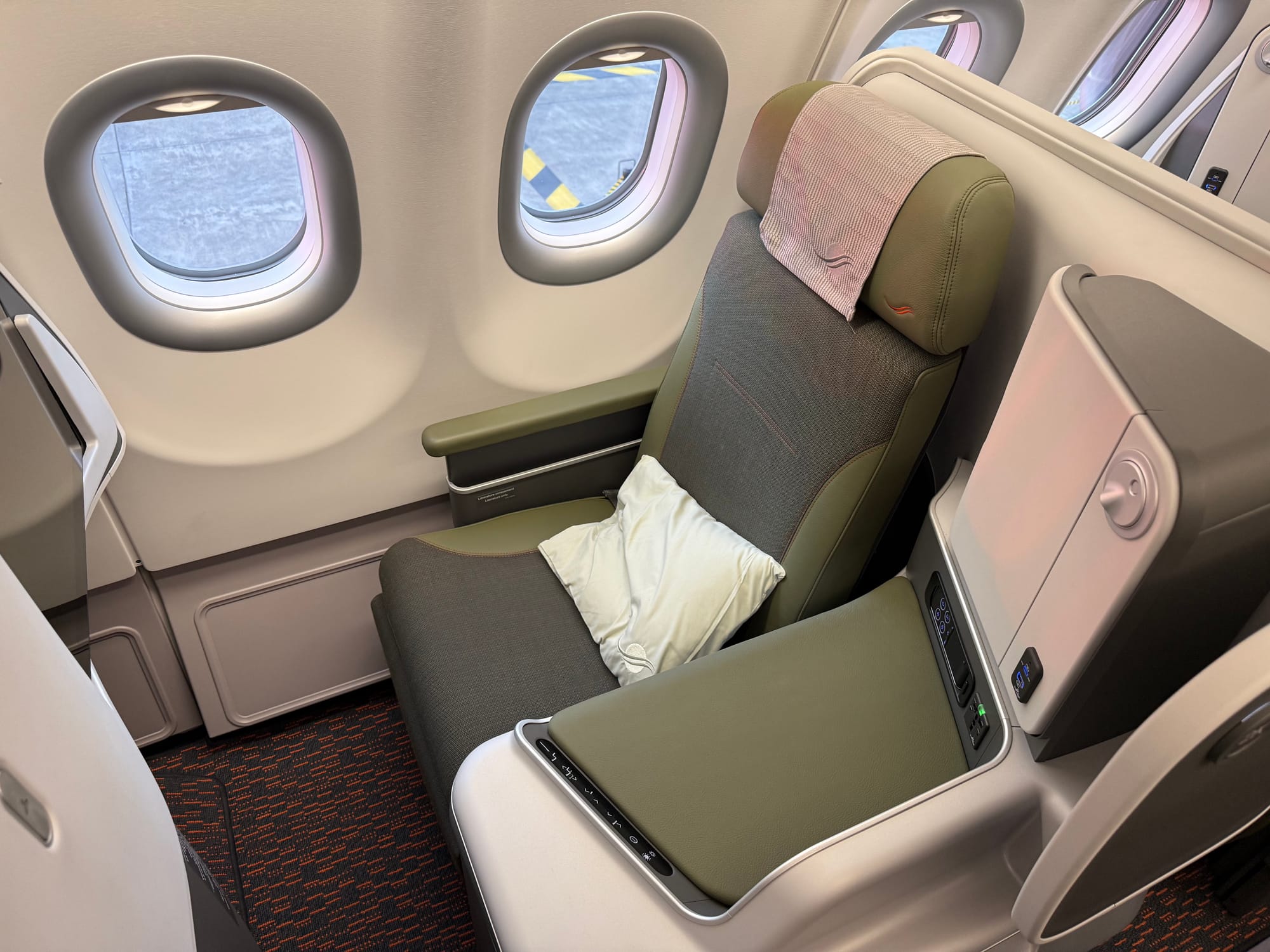 The window-adjacent seat, with dark green fabric in the centre and slightly lighter leather/leather-effect on the armrests, side table, and headrest.