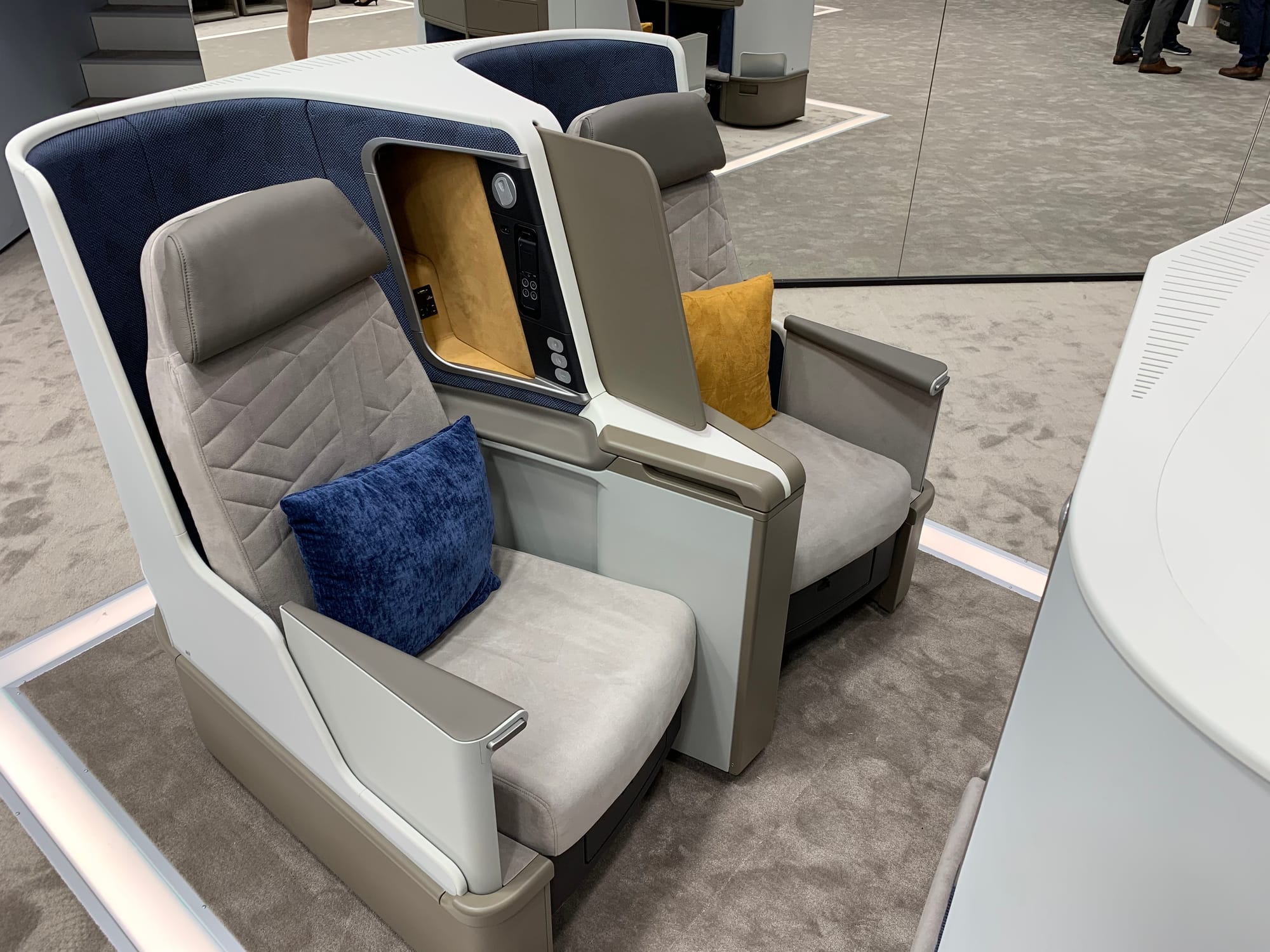 Seat on a trade show stand: a pair of together-facing flatbed seats in grey and blue with tan accents.