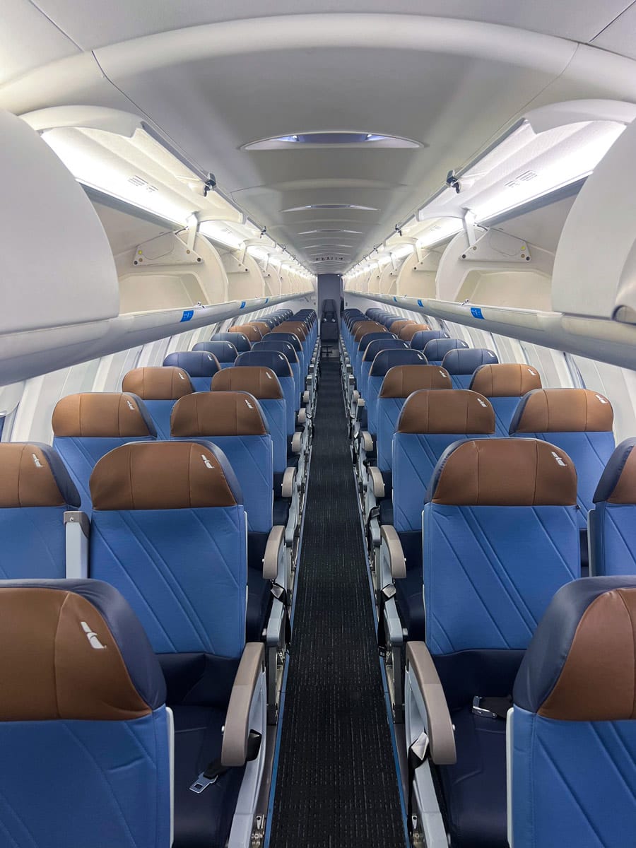Wide shot of the 2-2 economy section, but on a CRJ, where there are a few rows of brown headrests, then a few of blue, then a few more brown, then quite a few more blue. The seats in the foreground have visible puckering in several places on the backrest.