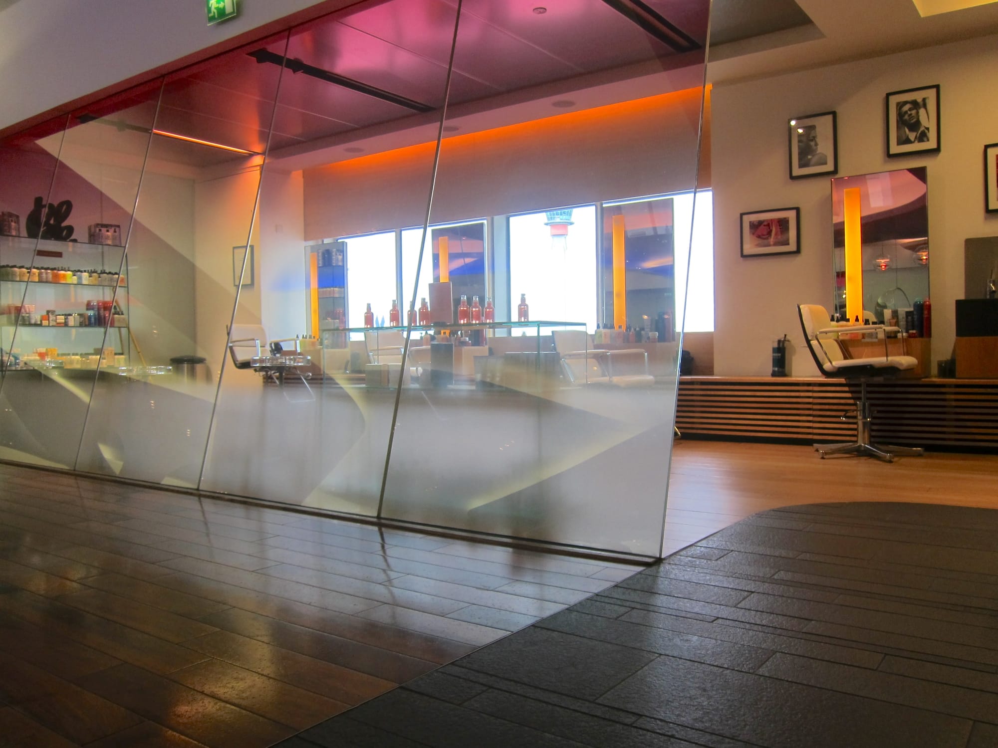 Interior, airline lounge, relatively low-res photo from the early 2010s in quality. Several hairdresser chairs sit in front of the windows and walls, behind slanting glass panels with pink tinting on top.