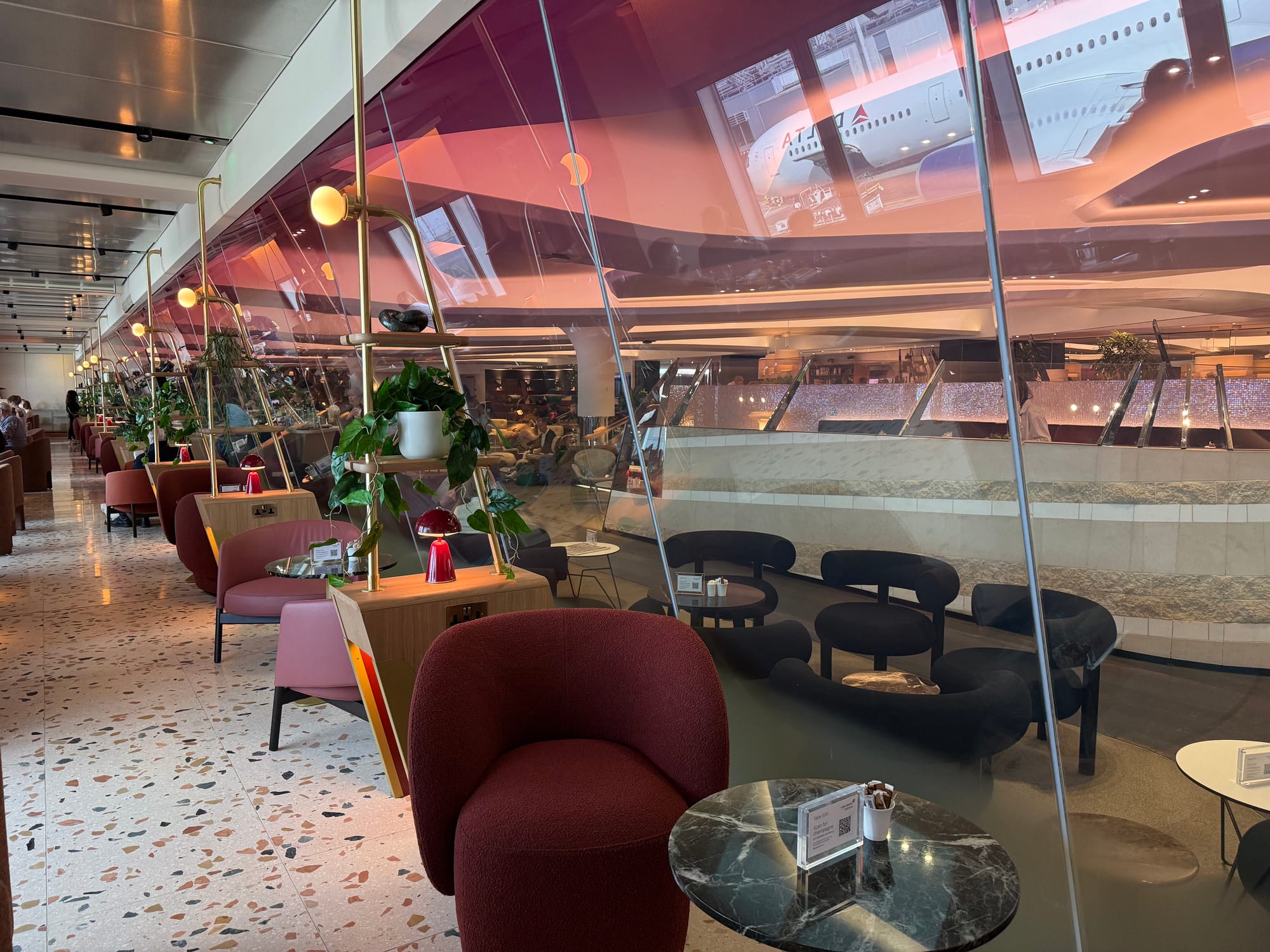 Interior, same lounge, daytime picture. Closeup on the seating on the right-hand side of the lounge, which is red and comes in different low chair options. At each space there is a power socket on a side table/lighting element.