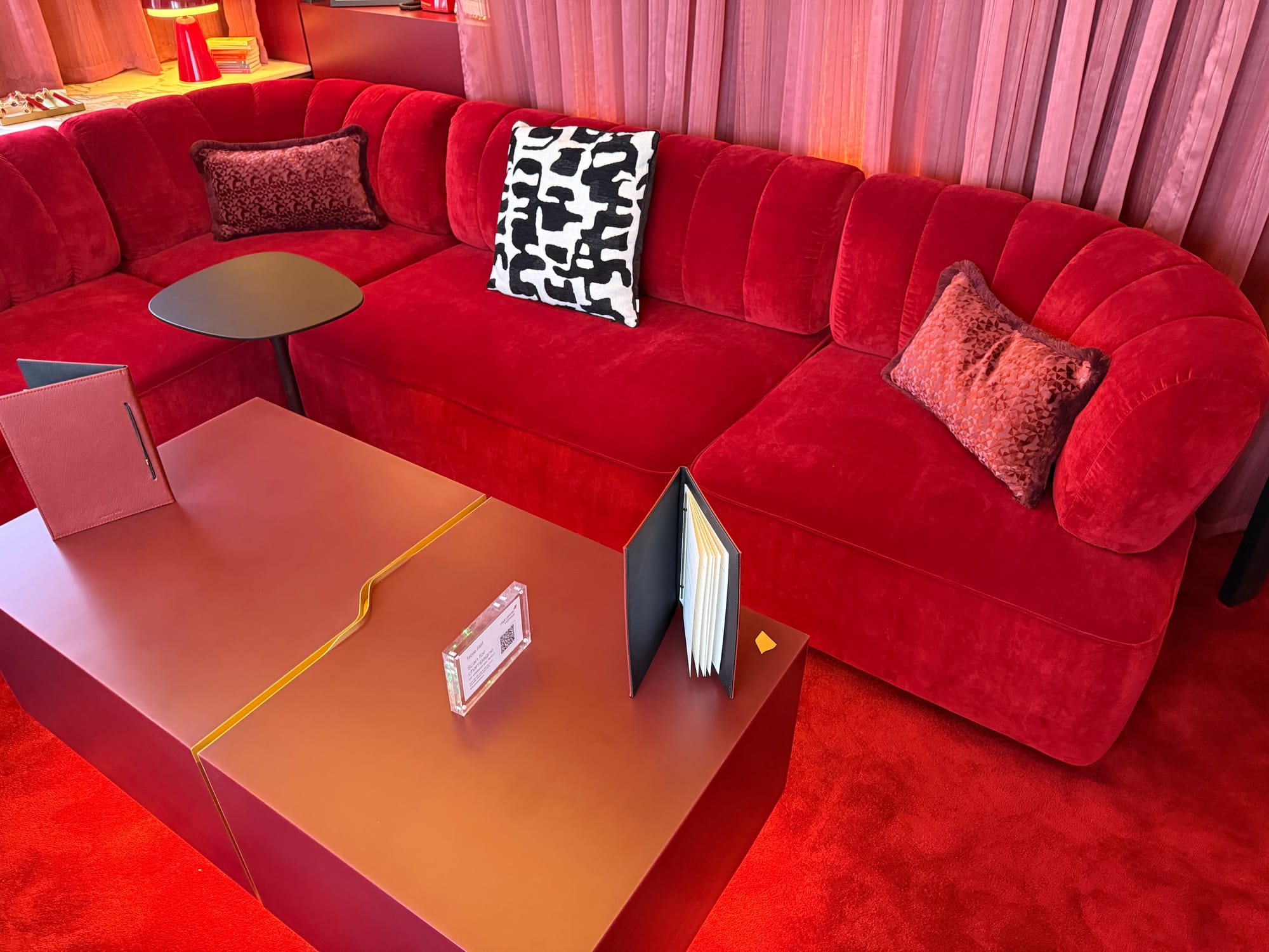 Interior, The Royal Box. Red everything: sheer curtains, velvety sofa, carpet, coffee table, lamp, plus a black side table and black-and-white pillow.