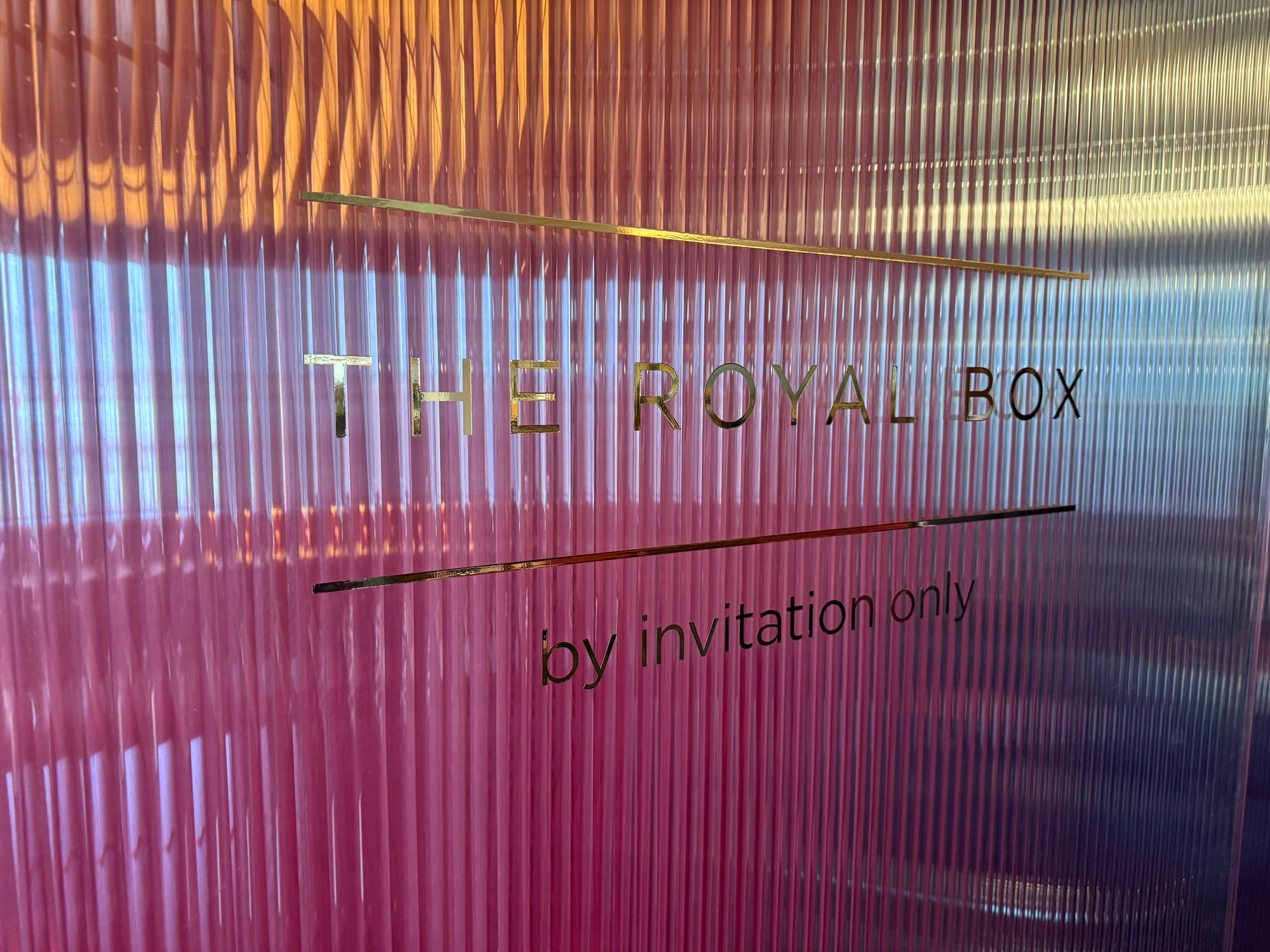 Closeup on a translucent pink-purple wall with “THE ROYAL BOX / by invitation only” printed on it.