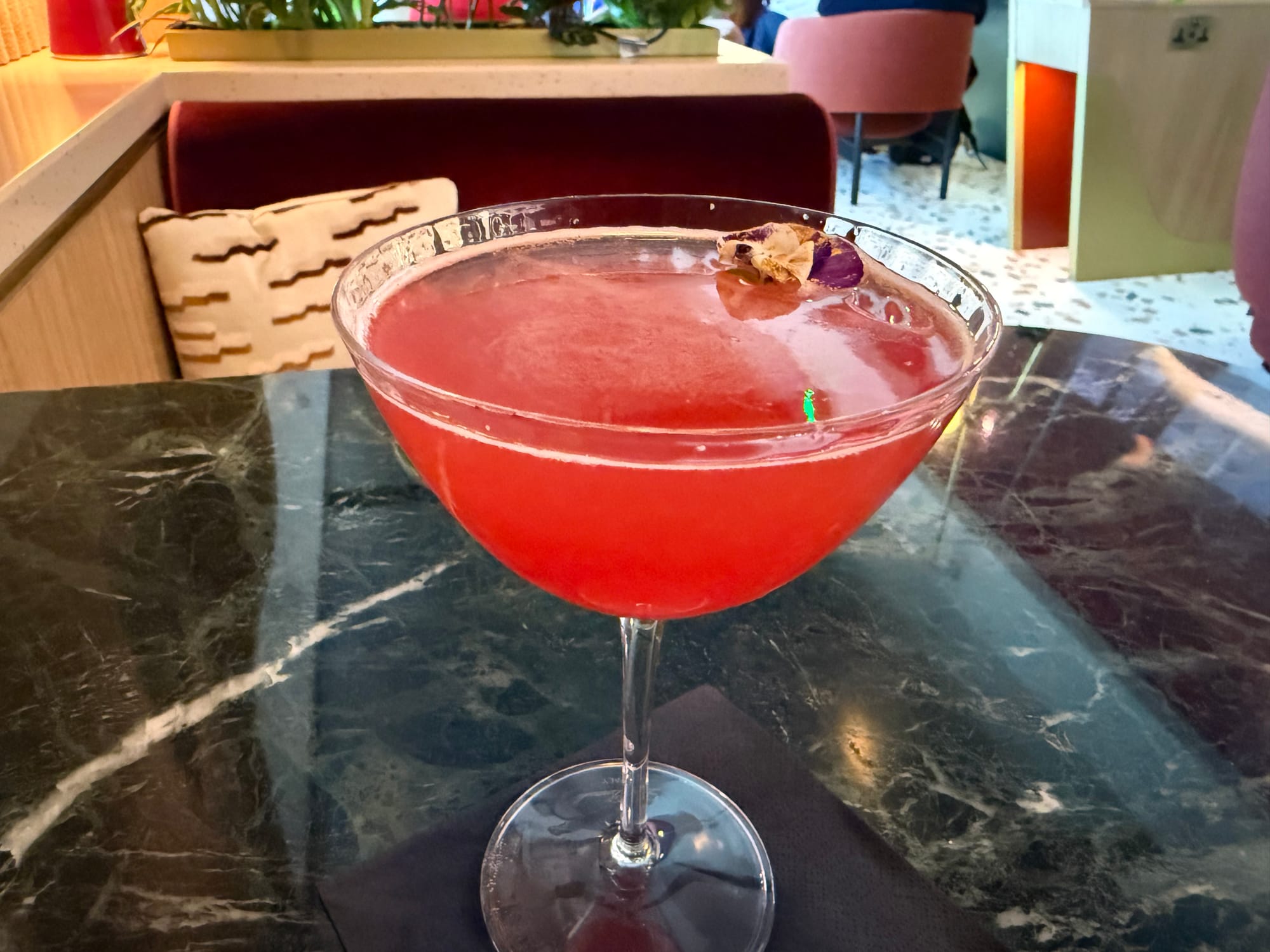 Closeup on a cocktail glass with a red cocktail, up, with a dried pansy on it.