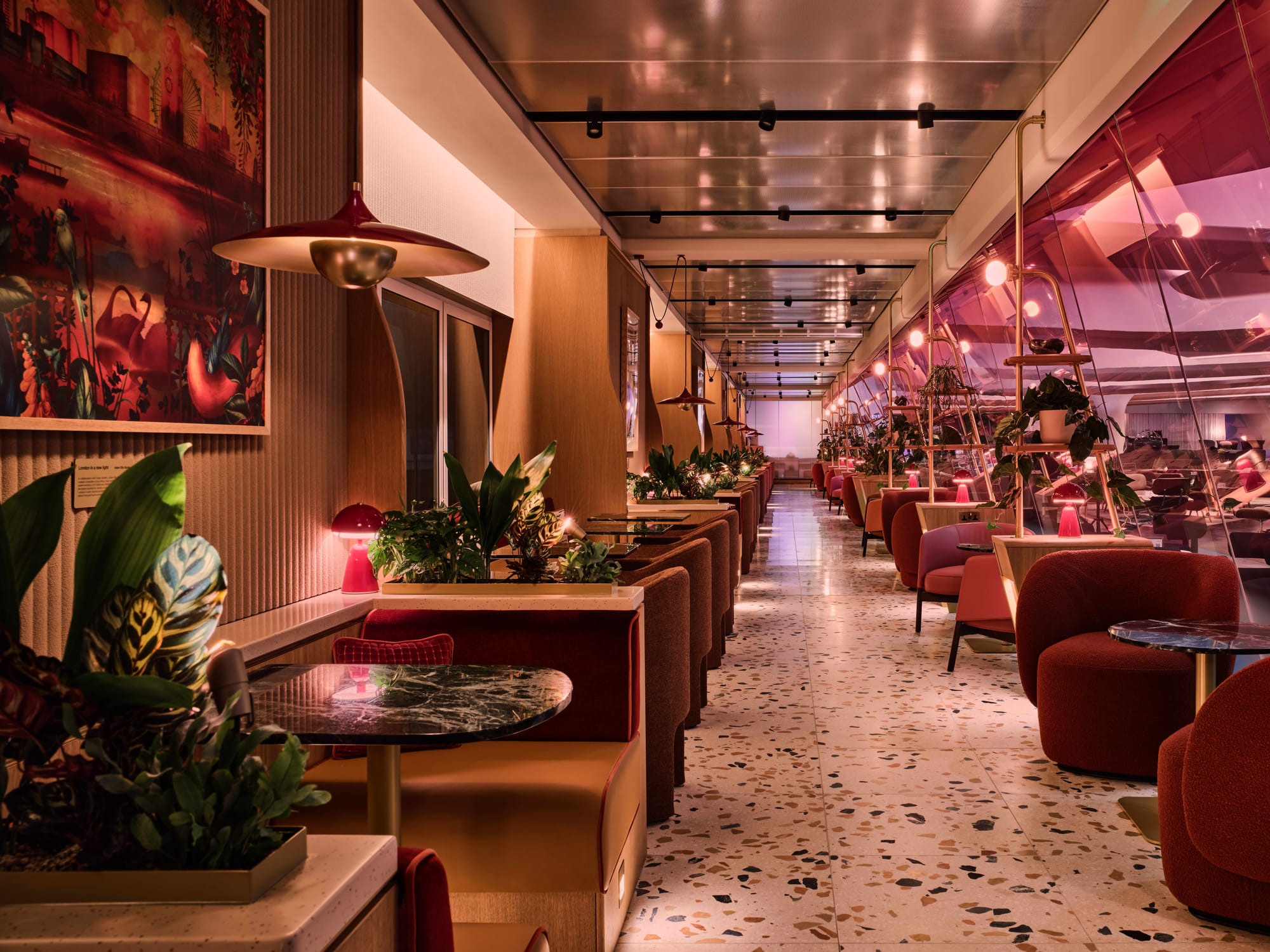 Modern photo of the same space, updated: terrazzo tile floors, welcoming red seating, booths with wooden elements, and separating gold light fixtures.