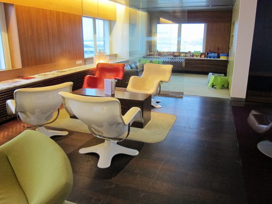 Slightly blurry, low-res early 2010s photo: a children’s play area with a few toys sits beyond four red/white scoop chairs at a table.