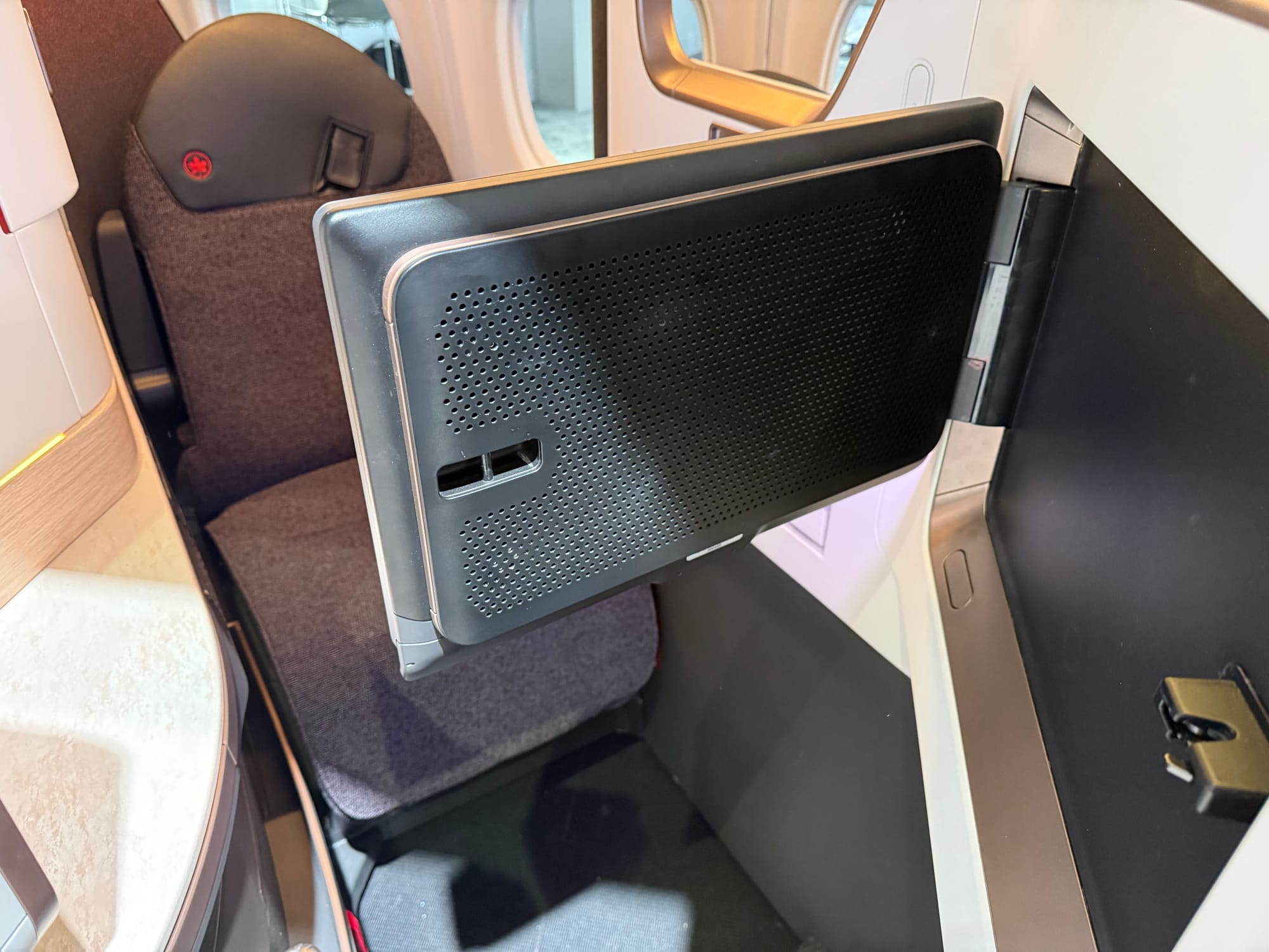 Looking down on the A321XLR Collins Aurora seat , with the rear of the monitor in view. It looks more attractive than you might expect, with a bronze ring around it plus a perforated plastic back.