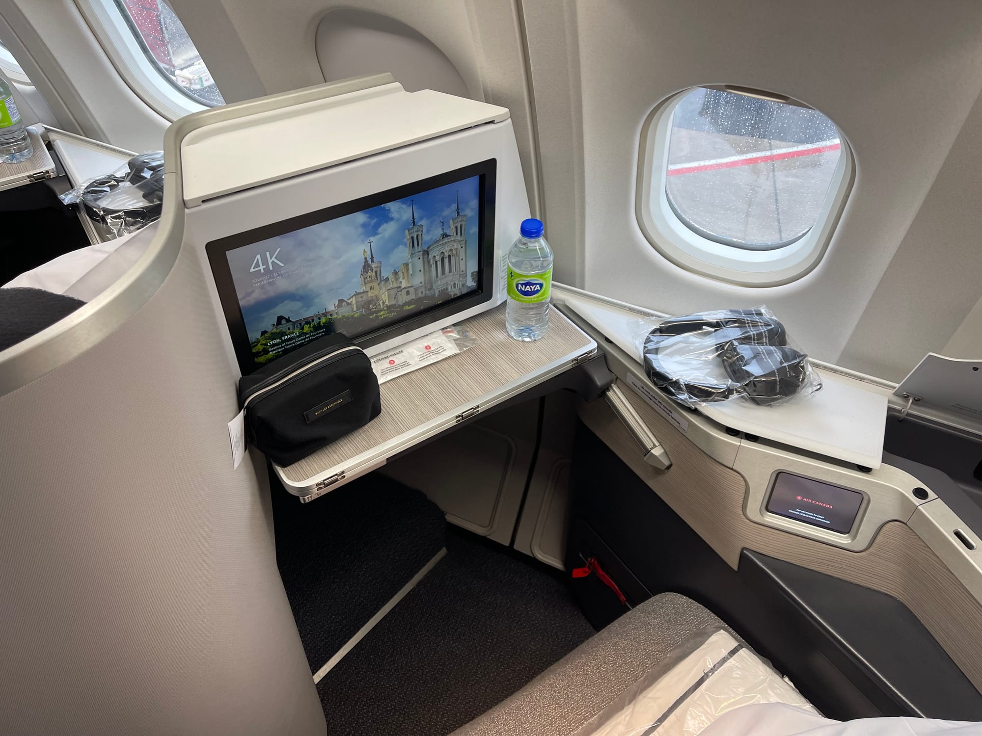 A view from above and slightly behind a Collins Aerospace Super Diamond seat on an A330. It is almost entirely greys and beiges. The only pops of colour are the lifejacket tab adn a tiny Air Canada logo on the seat control screen.