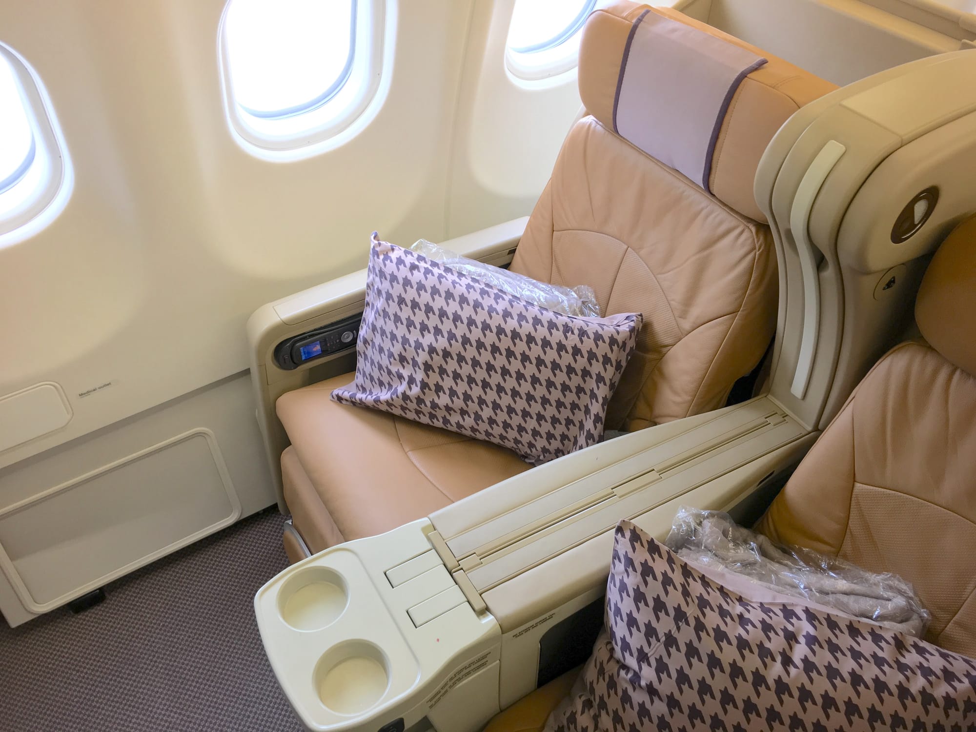 Beige-coloured angled lie-flat seat with a Singapore Airlines signature cushion.