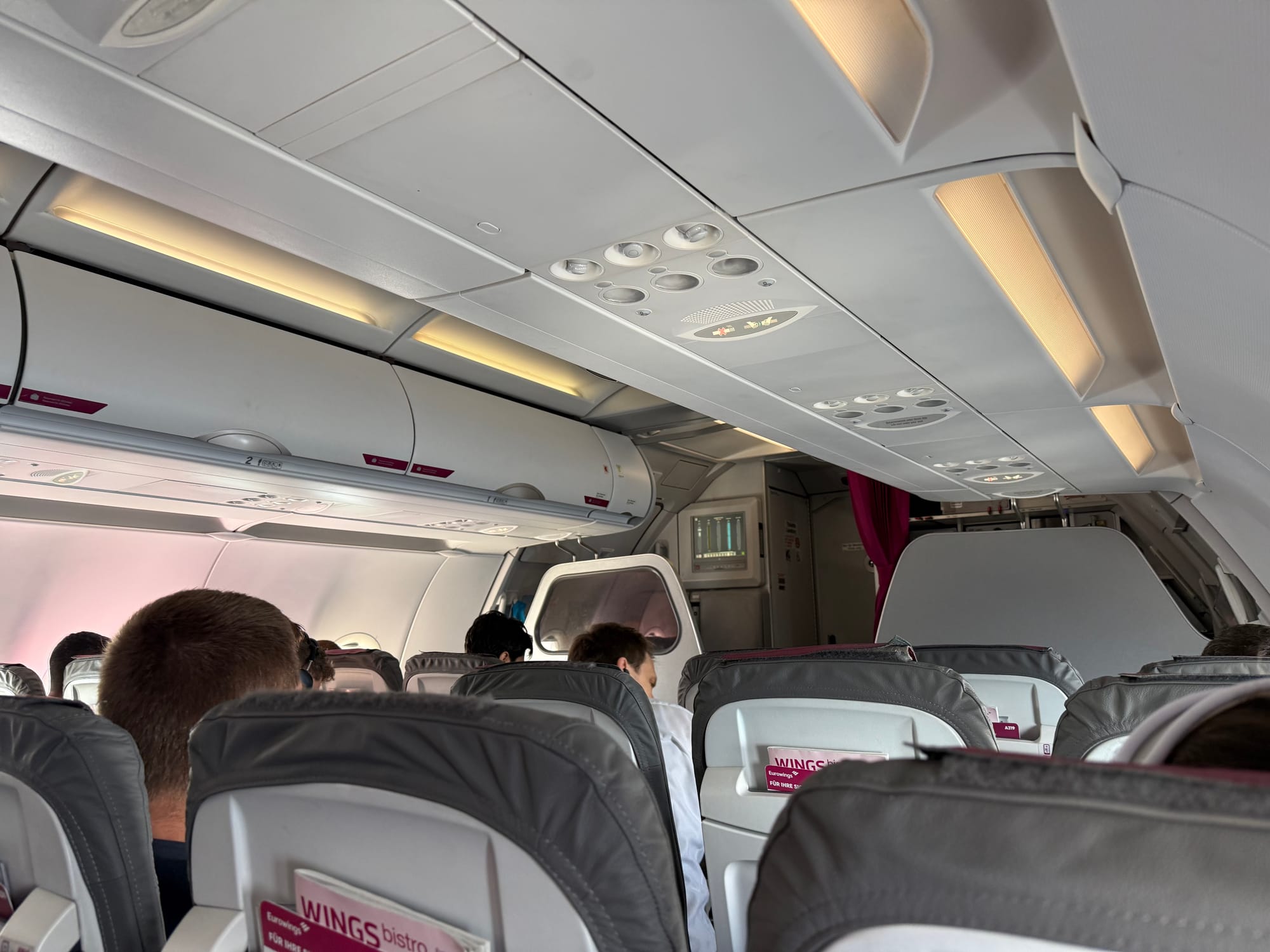 Looking forward fro the fourth row of an A320ceo family aircraft, with slimline grey seats and a thin divider between the flight attendant seats and the front row of passengers.