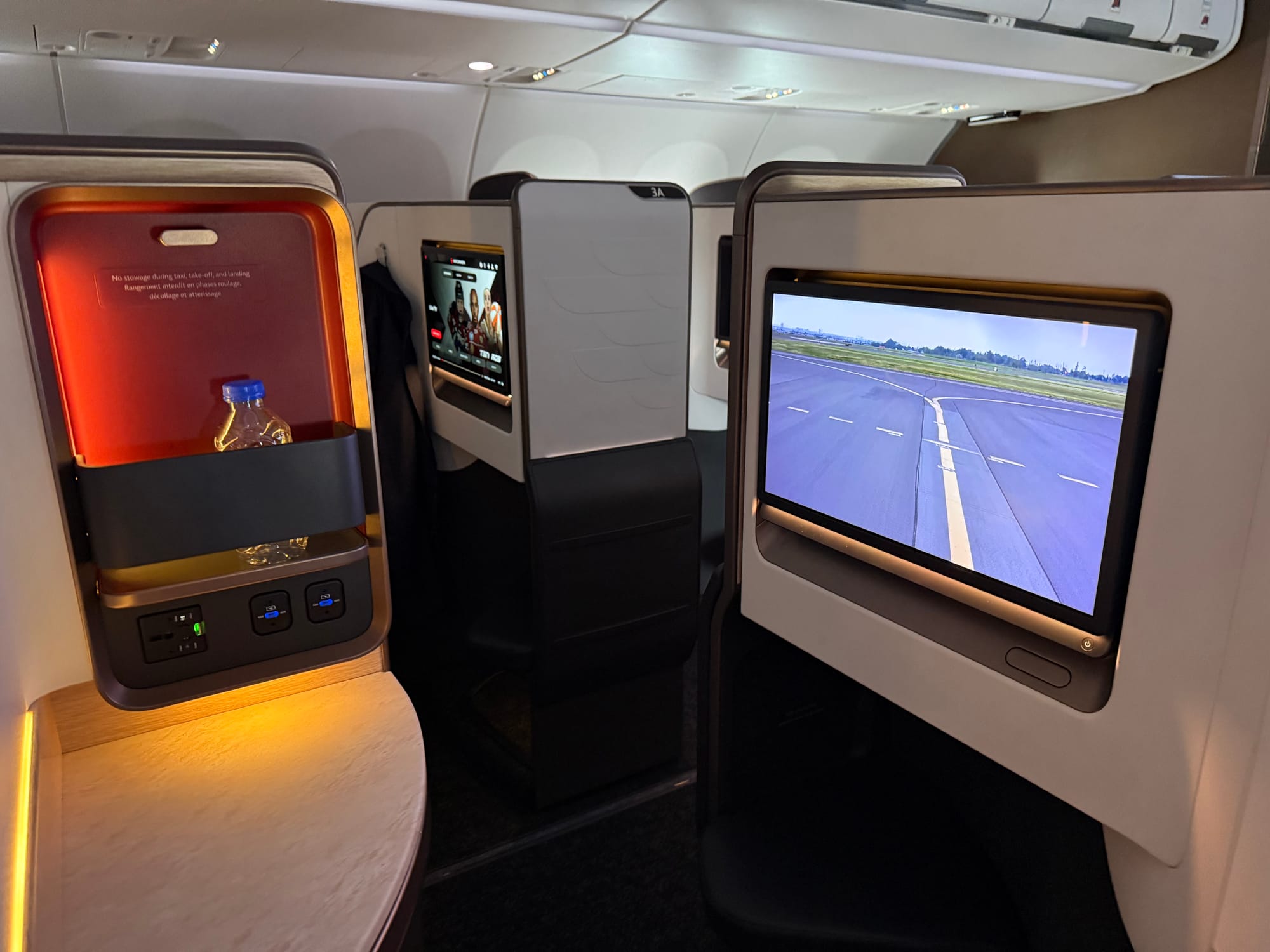 A view out of the seat at the large, stylish screen on the right and a storage area with power (2x USB-C, 1 AC). You can just about see the (stowed) screen of the passenger opposite, but by no means the passenger themself.