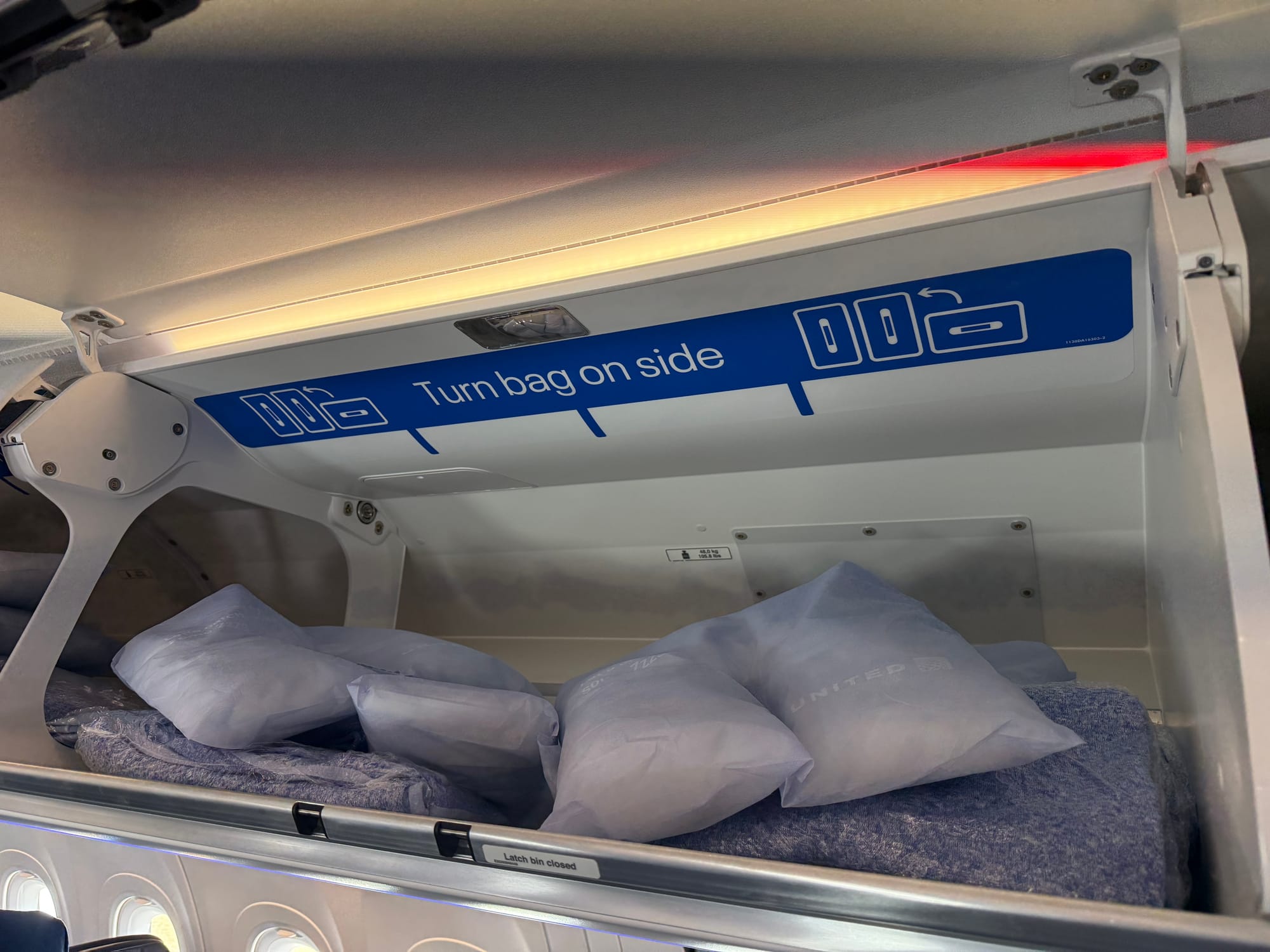 Interior, overhead bin, with large placard demonstrating how to (and stating) “turn bag on side”.