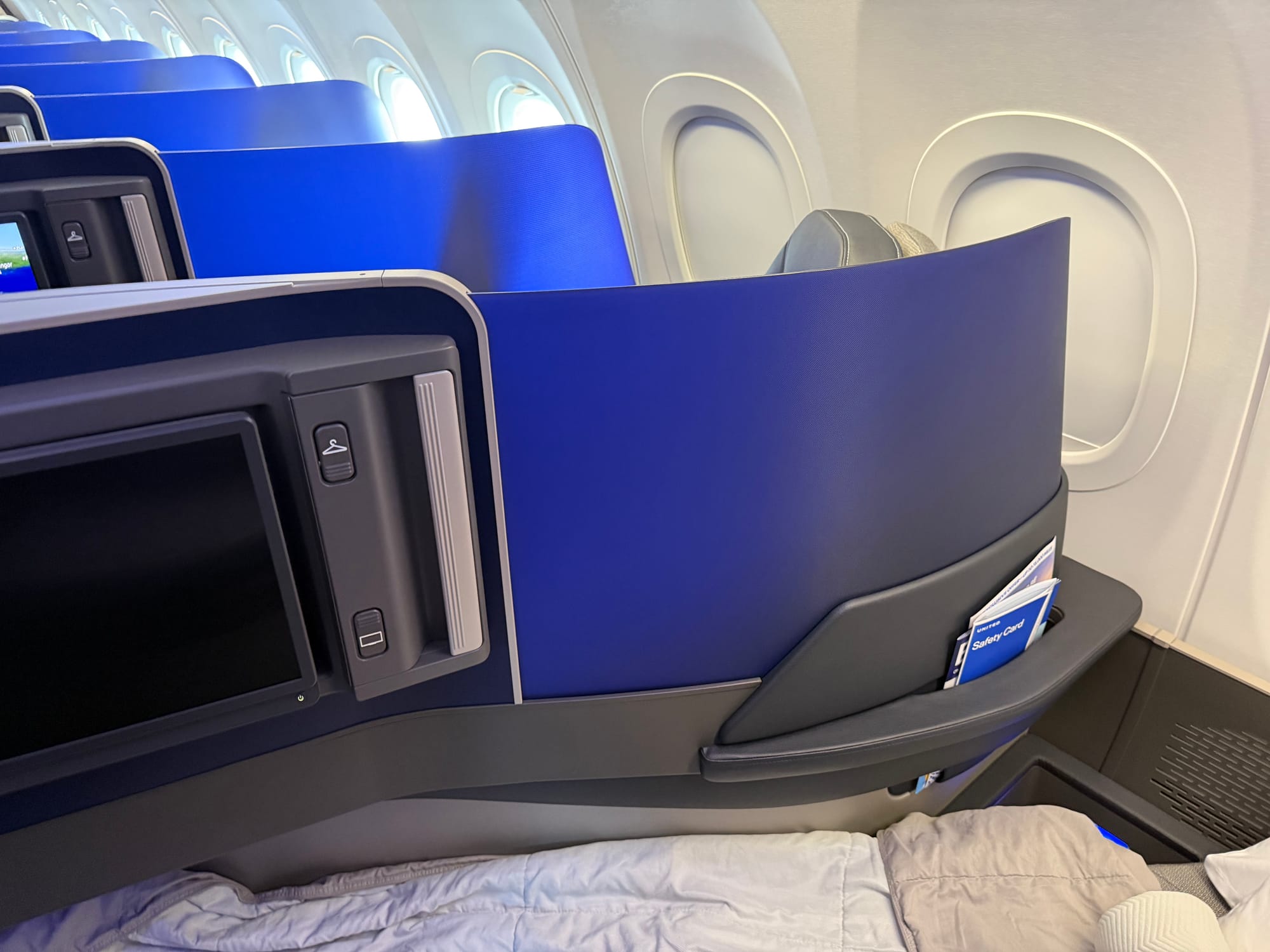 A view of the seat in bed mode, but focussing on the divider and a pair of buttons approx 2cm wide and 3cm high, one about 15cm above the other. The top one has a coathanger symbol, the bottom has a monitor symbol.
