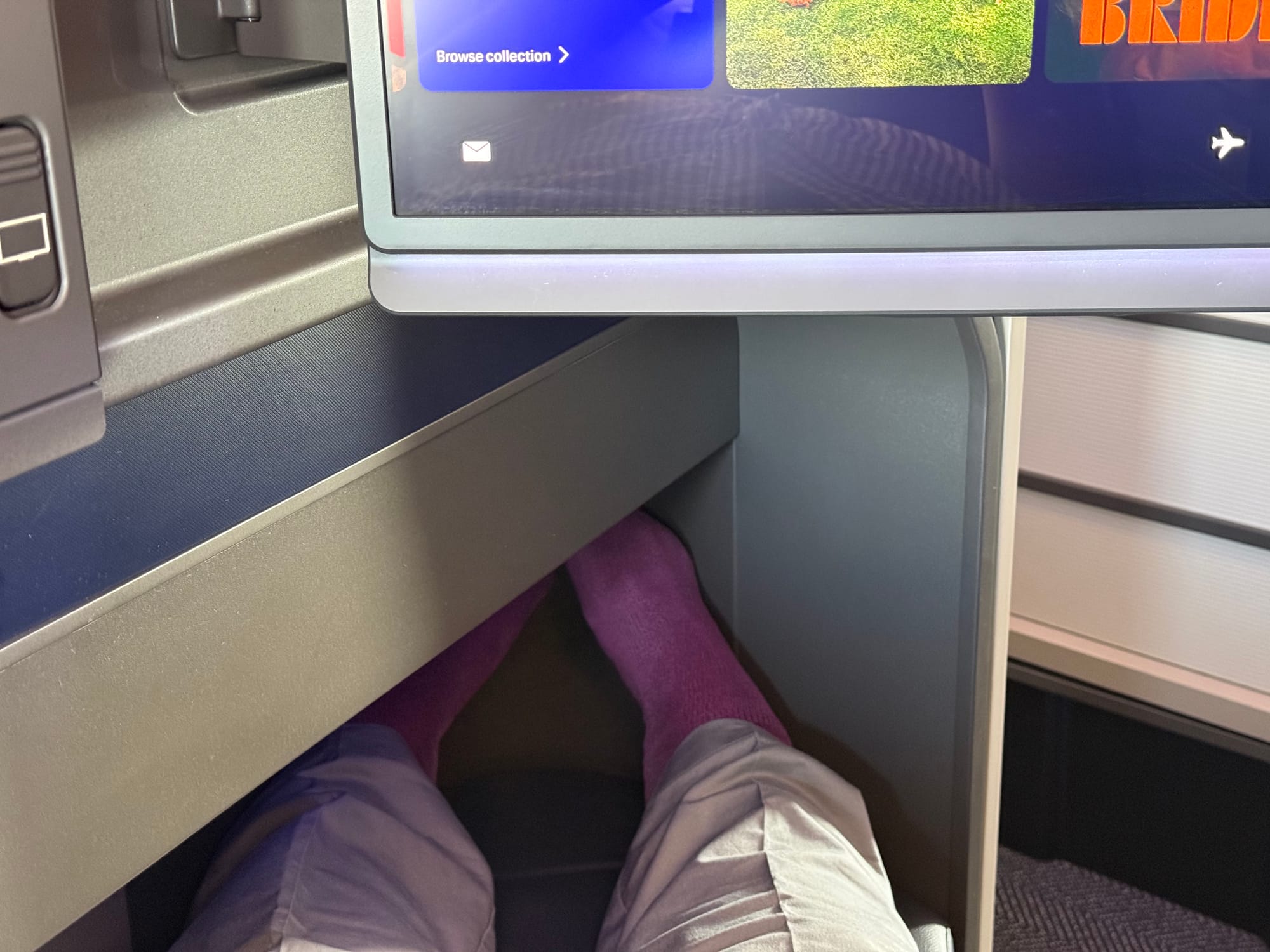 Closeup on the footwell with two trousered legs and purple-socked feet looking a bit cramped.