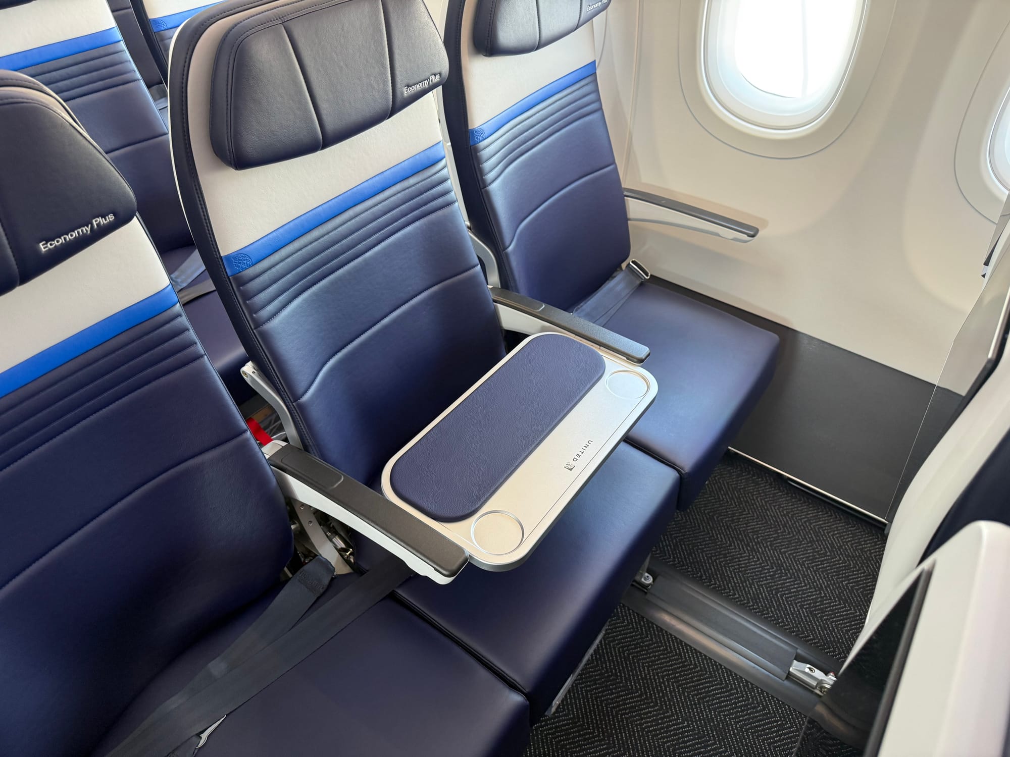 Blue and grey economy seats marked Economy Plus. The middle one has a table between the armrests.