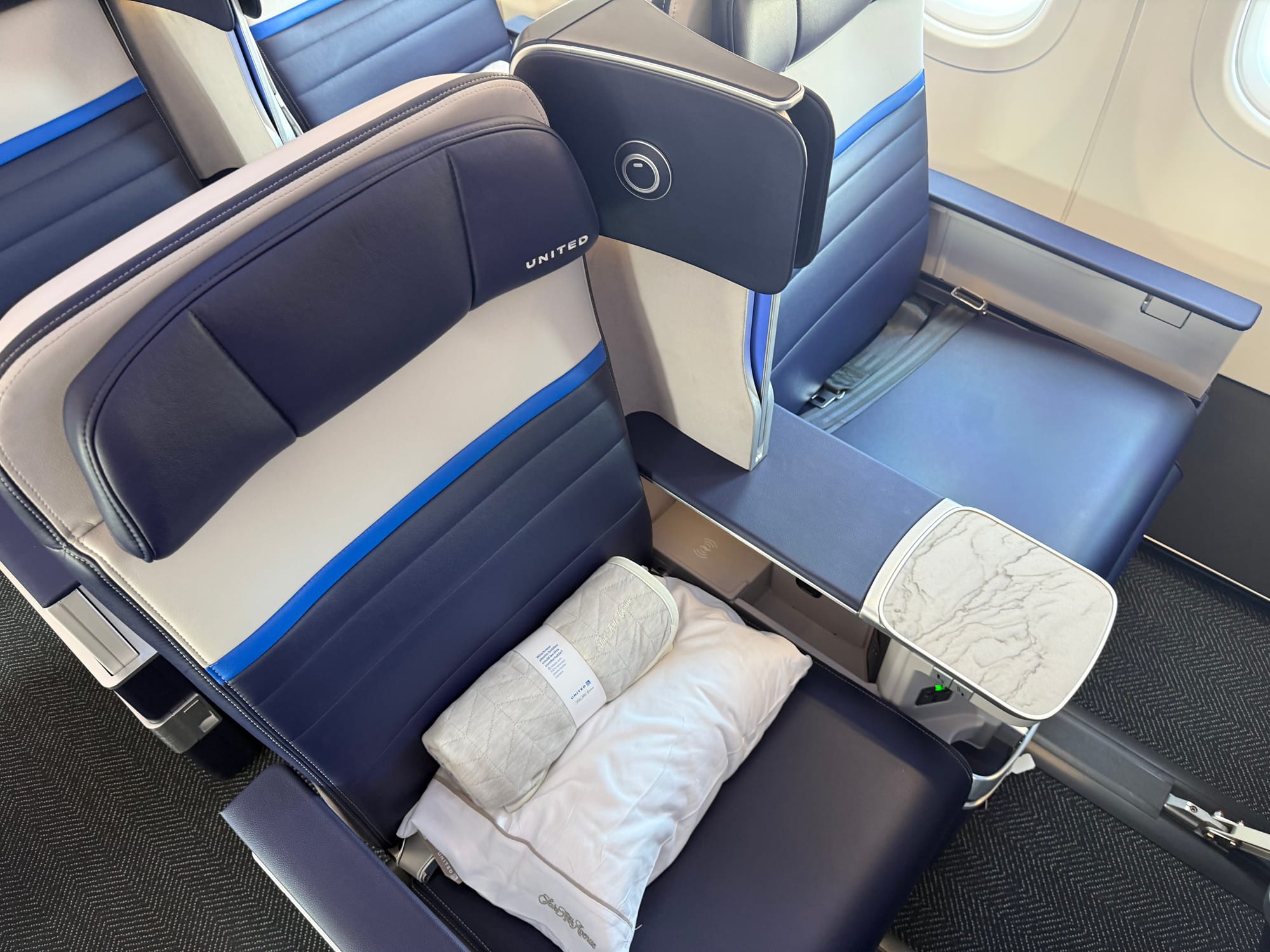 Two blue and grey premium economy recliner seats, with a stone cocktail table and a dividing privacy element between them.