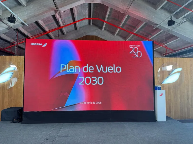 Interior, warehouse type building. Big screen reads: Iberia / Plan de Vuelo 2030