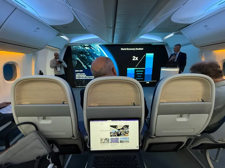 Interior, Boeing 777X mockup cabin, second row of economy, with a slide on the main screen and a man presenting