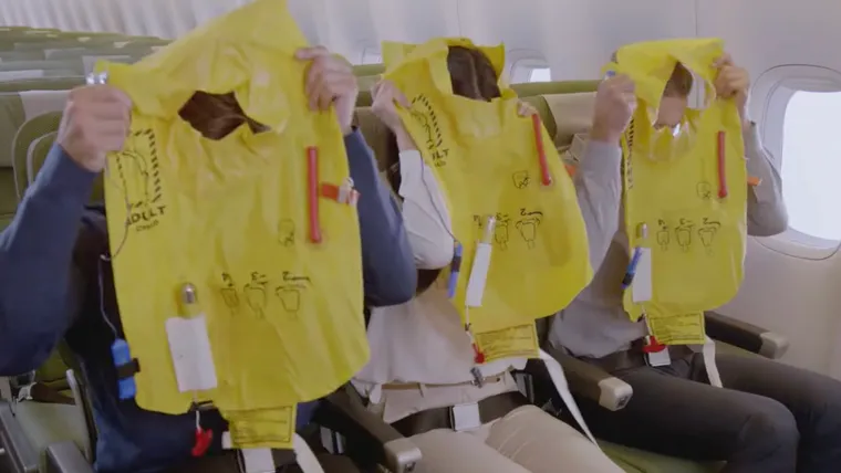 Screenshot, Qantas safety video. Three passengers are putting their lifejackets on.