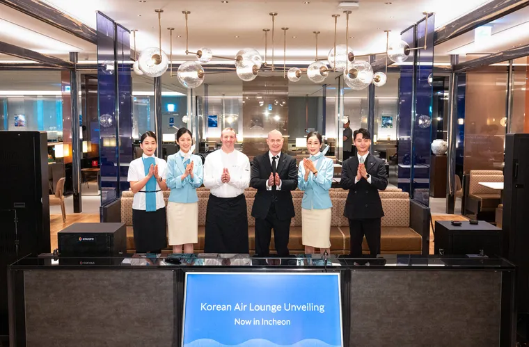 Interior, lounge. Six people celebrate behind a sign that says "Korean Air Lounge Unveiling"