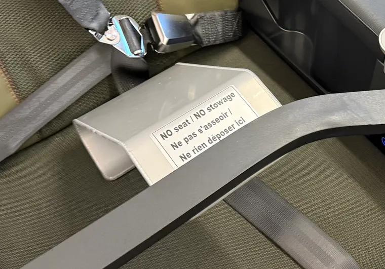 Closeup, premium economy seat. A bar with the placard "NO seat / NO stowage" (also in French).
