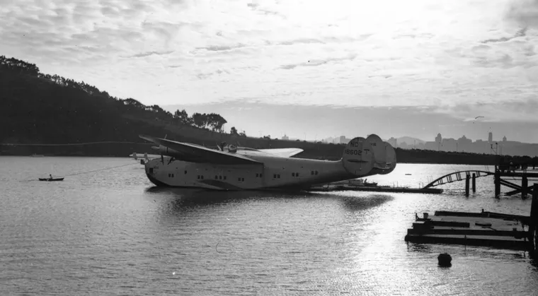 a large seaplane sitting on the water, beneath a sunset.