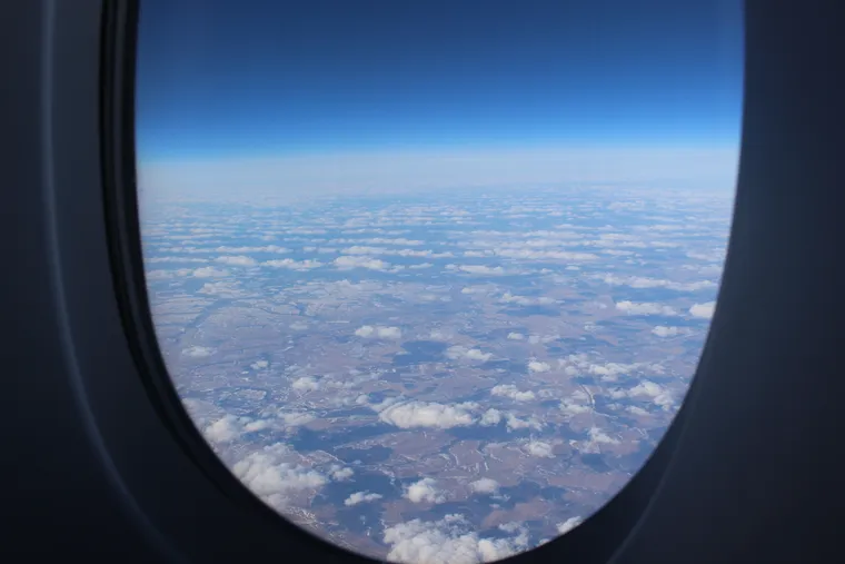 A view from an airplane window of some slightly snowy flat land with fields, with light clouds.