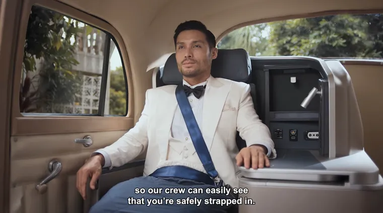 Screenshot, safety video. A man is belted into a business seat, but set in an old limo.