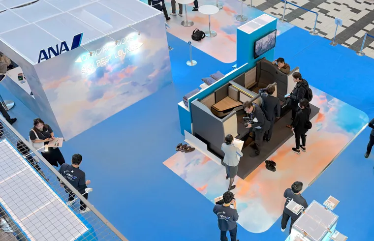 The Room FX mockup on an event stand, with ANA branding band signs to “Official Goods” and “Sky Rest” lounge beyond.