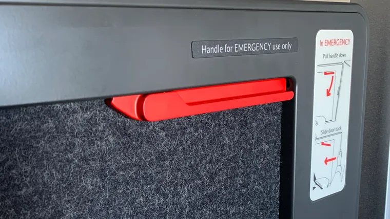 Closeup on a red handle inside a business class suite. Two placards note “Handle for EMERGENCY use only” and “in EMERGENCY Pull handle down/Slide door lock”