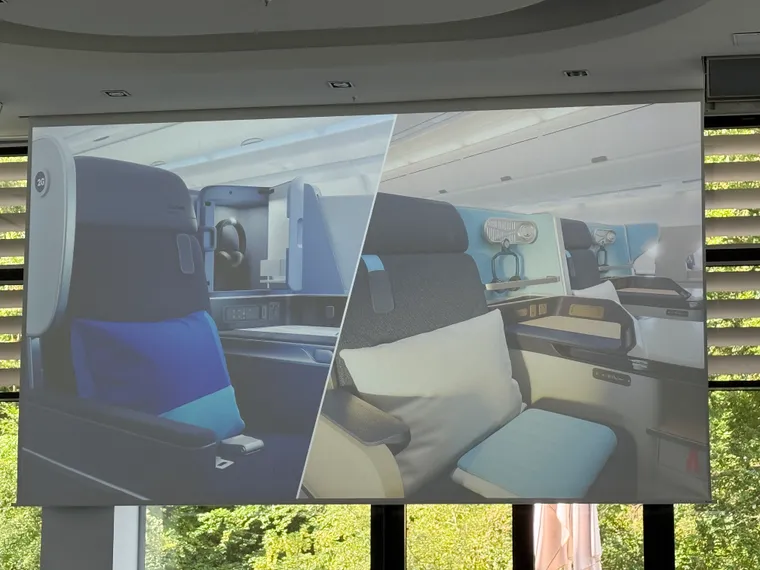 Photo of a projector screen: two very similar Thompson Vantage XL/XL+ staggered business class seats in shades of blue