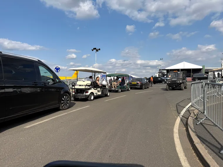 Buggies, cars and vans on the roads at the Farnborough Airshow, with one yellow DHL 777 visible beyond.